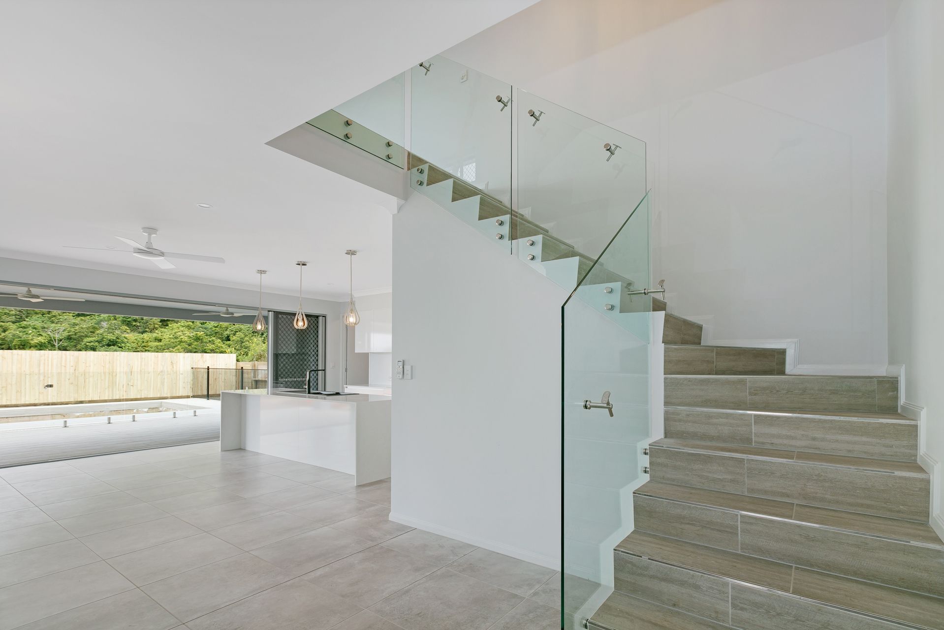 A Modern Interior Featuring a Glass-railed Staircase With Grey Tiled — Ashlee Jones Homes in Gordonvale, QLD