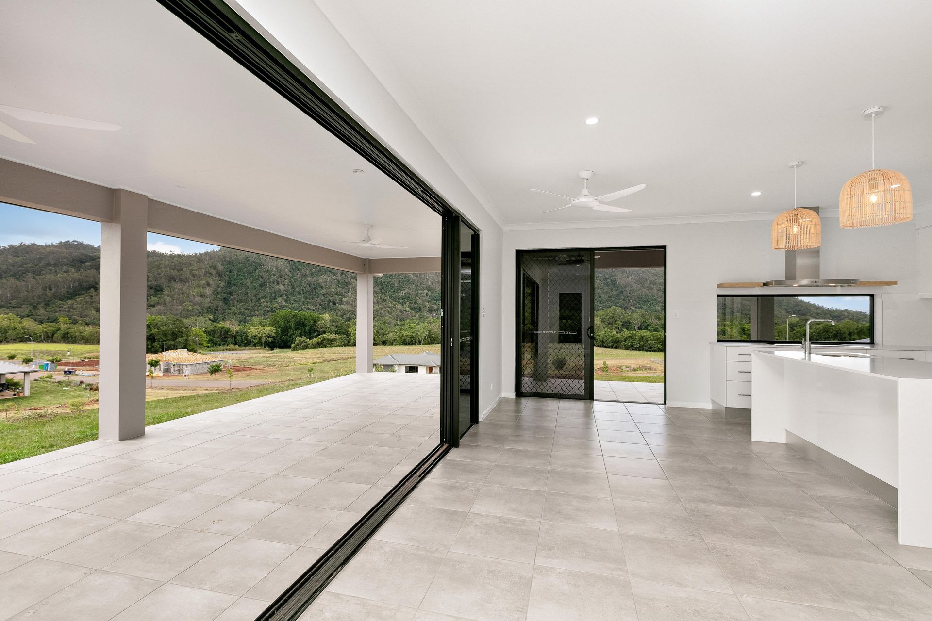 A Modern Open-plan Living Area With Light Tile Floors, a White Kitchen — Ashlee Jones Homes in Gordonvale, QLD