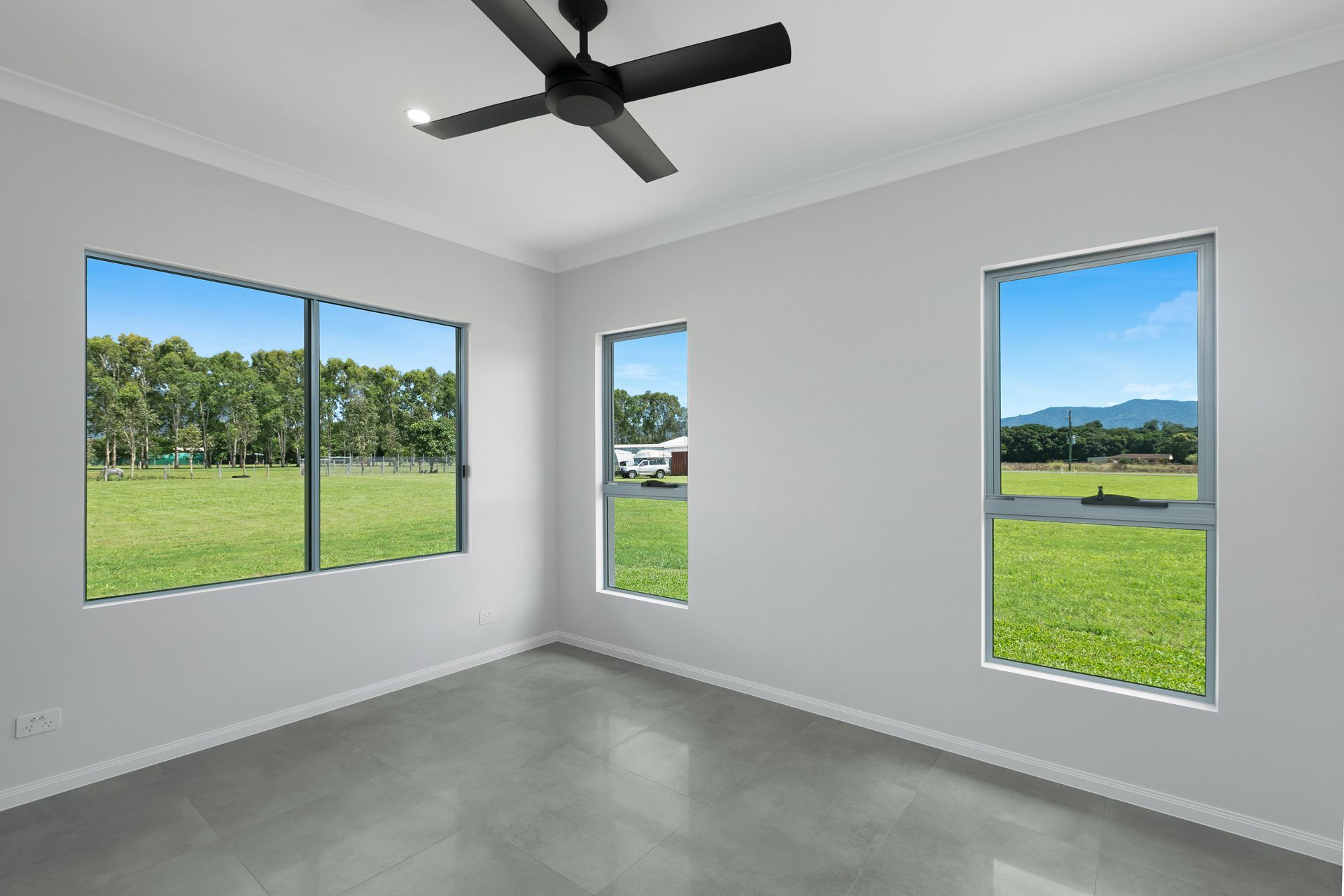 Empty Room With Gray Floors, White Walls, a Ceiling Fan, and Large Windows — Ashlee Jones Homes in Gordonvale, QLD