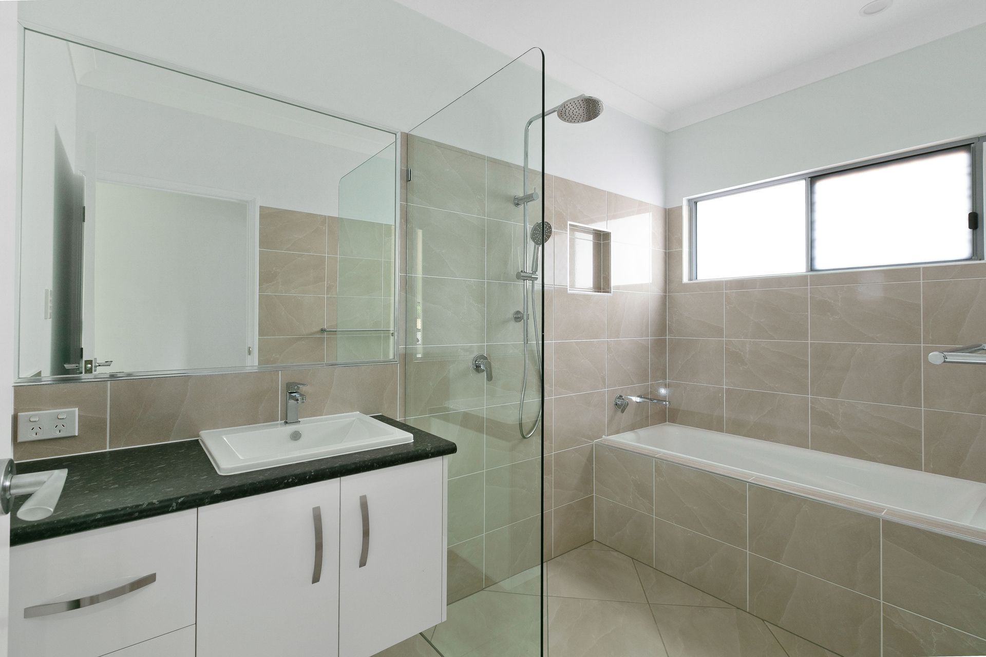 A Modern Bathroom Featuring a White Vanity With a Dark Countertop — Ashlee Jones Homes in Gordonvale, QLD