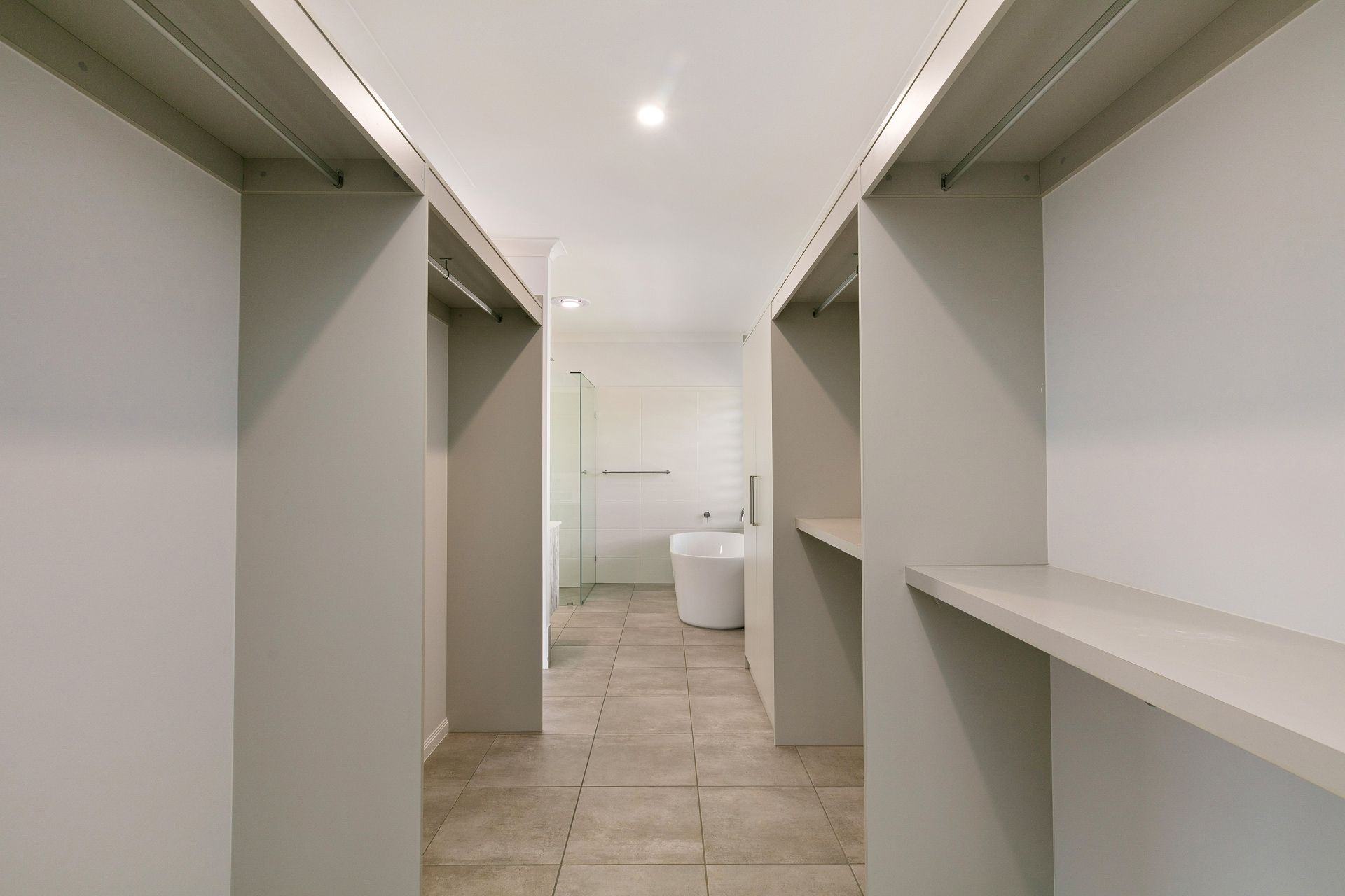 A Walk-through Closet With Light Grey Walls and Shelves — Ashlee Jones Homes in Gordonvale, QLD