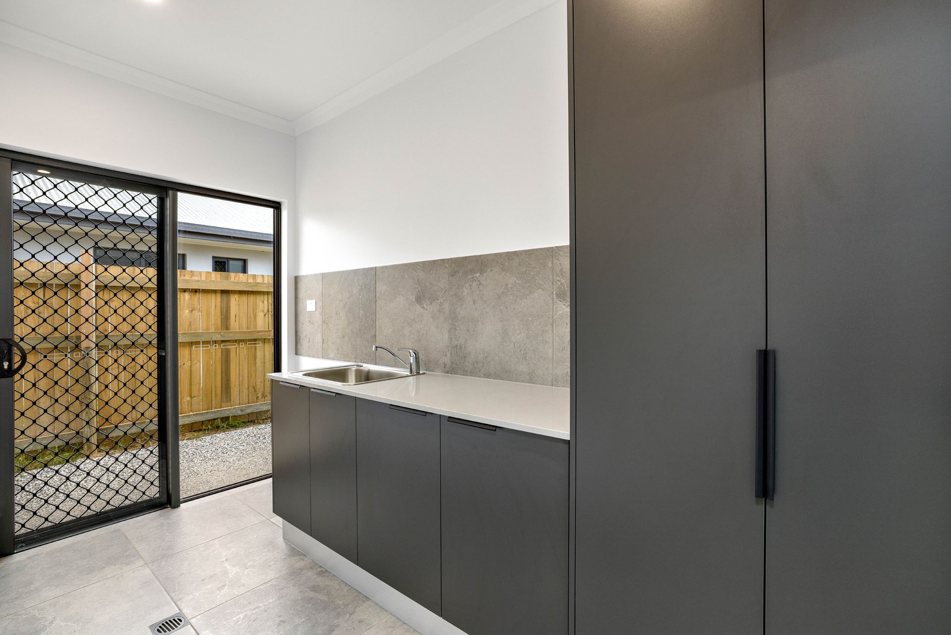 A Modern Laundry Room With Dark Grey Cabinets, a Sink — Ashlee Jones Homes in Gordonvale, QLD