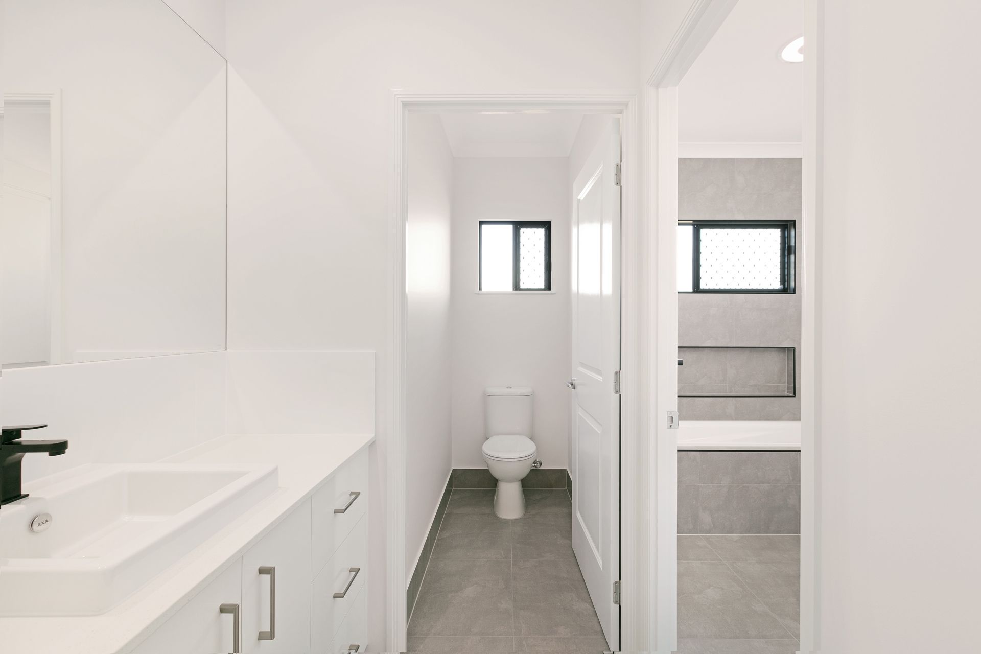A Bright, Modern Bathroom Featuring a White Vanity With a Black Faucet — Ashlee Jones Homes in Gordonvale, QLD