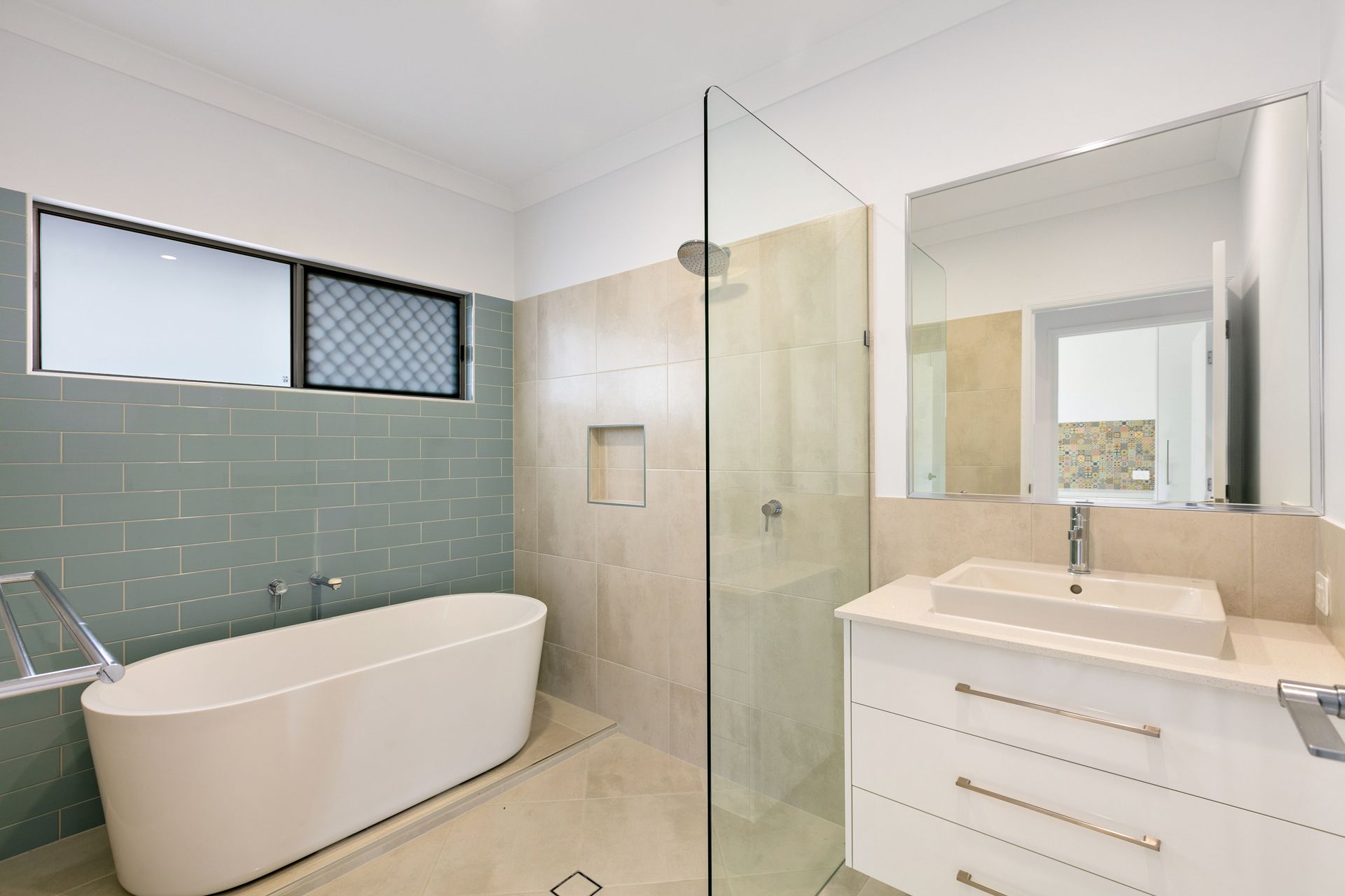 A Modern Bathroom Featuring a White Freestanding Bathtub Against Sage Tiles — Ashlee Jones Homes in Gordonvale, QLD