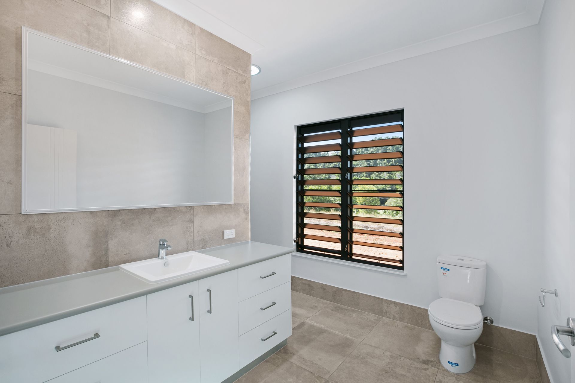 A Bright Bathroom With a White Vanity, Large Mirror — Ashlee Jones Homes in Gordonvale, QLD
