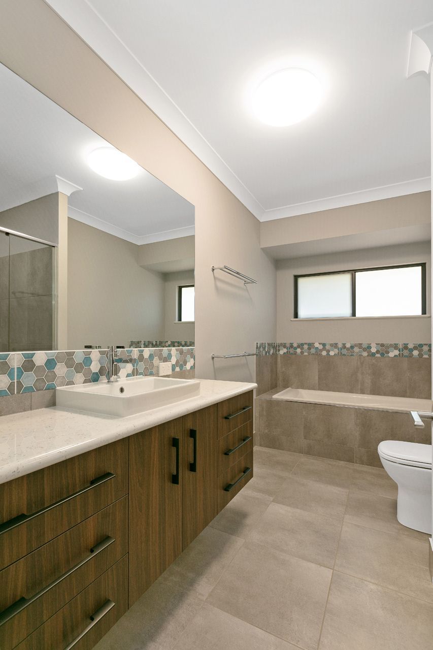 A Modern Bathroom With a Wooden Vanity, a Large Mirror — Ashlee Jones Homes in Gordonvale, QLD
