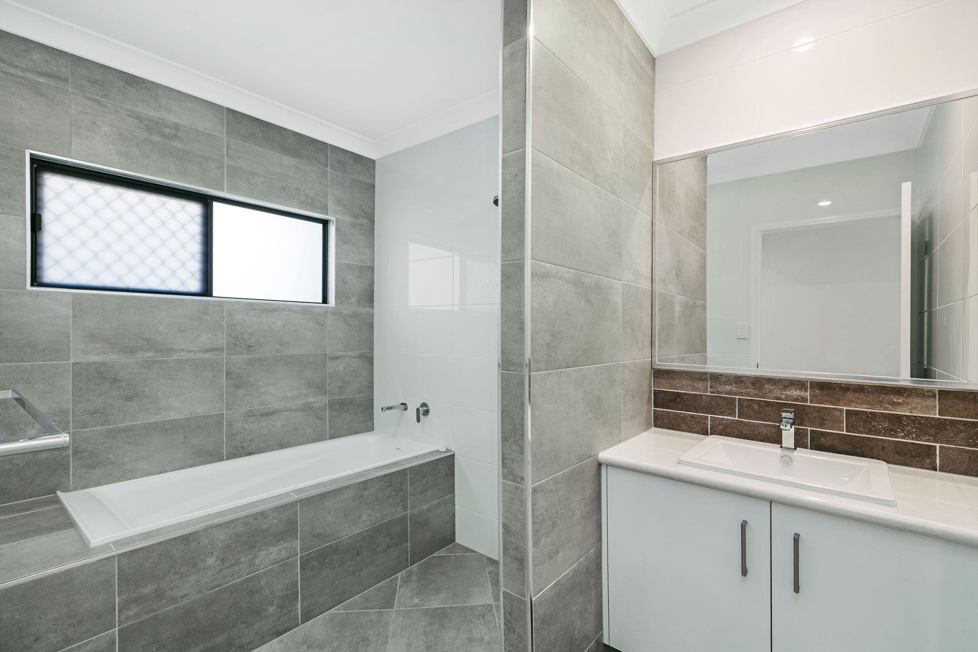A Modern Bathroom Featuring a White Bathtub, Grey Wall Tiles — Ashlee Jones Homes in Gordonvale, QLD