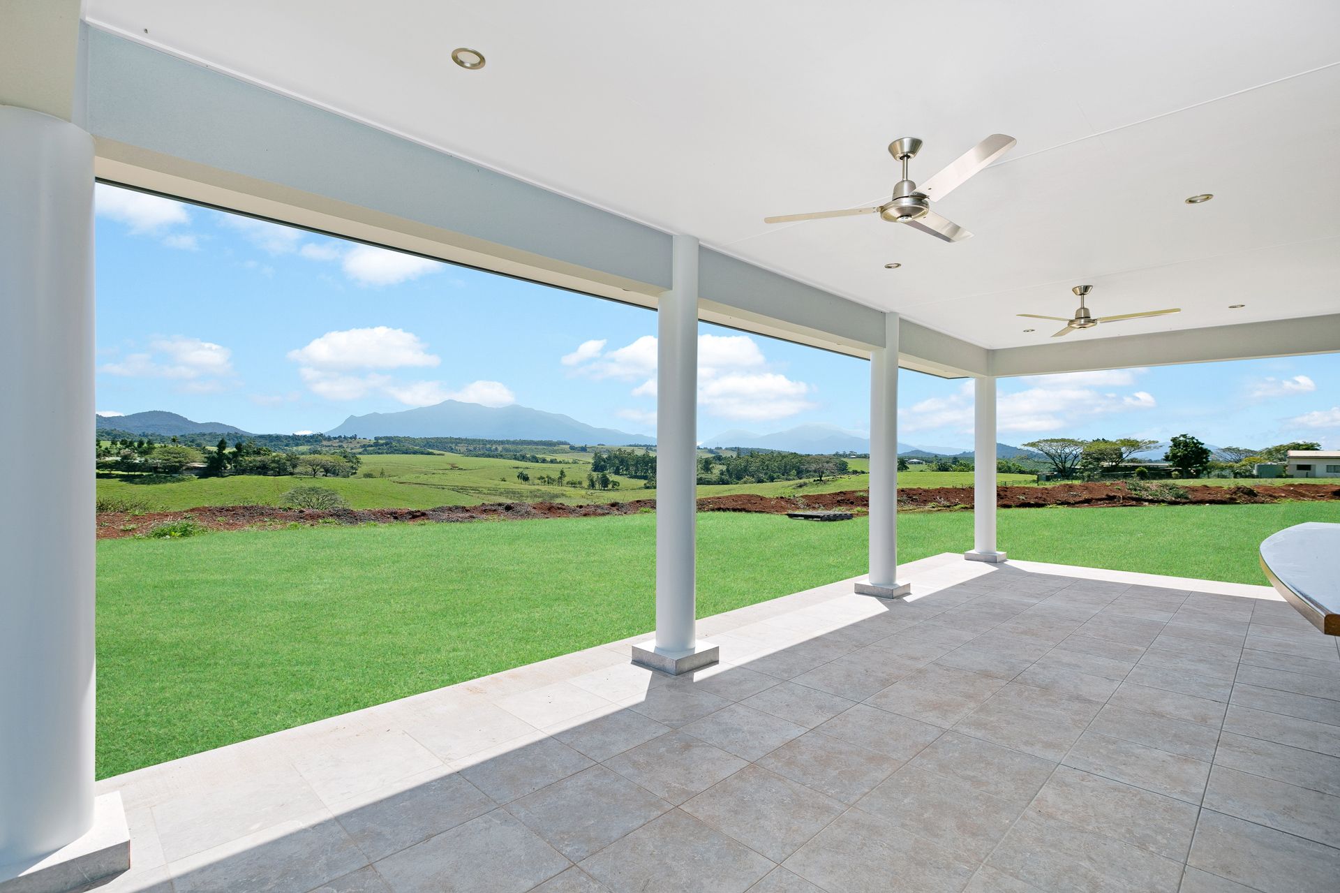A Bright, Covered Patio With White Pillars and Ceiling Fans — Ashlee Jones Homes in Gordonvale, QLD