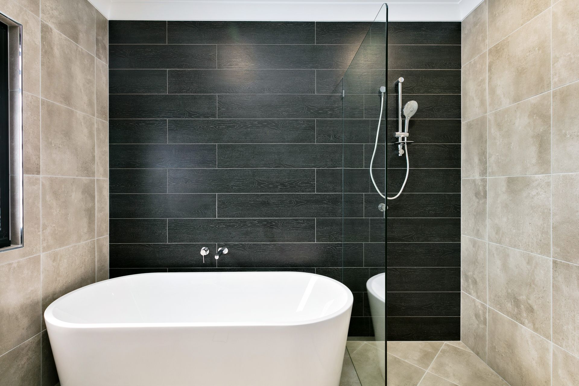 A White Freestanding Bathtub Positioned in Front of a Dark Tiled Feature Wall — Ashlee Jones Homes in Gordonvale, QLD