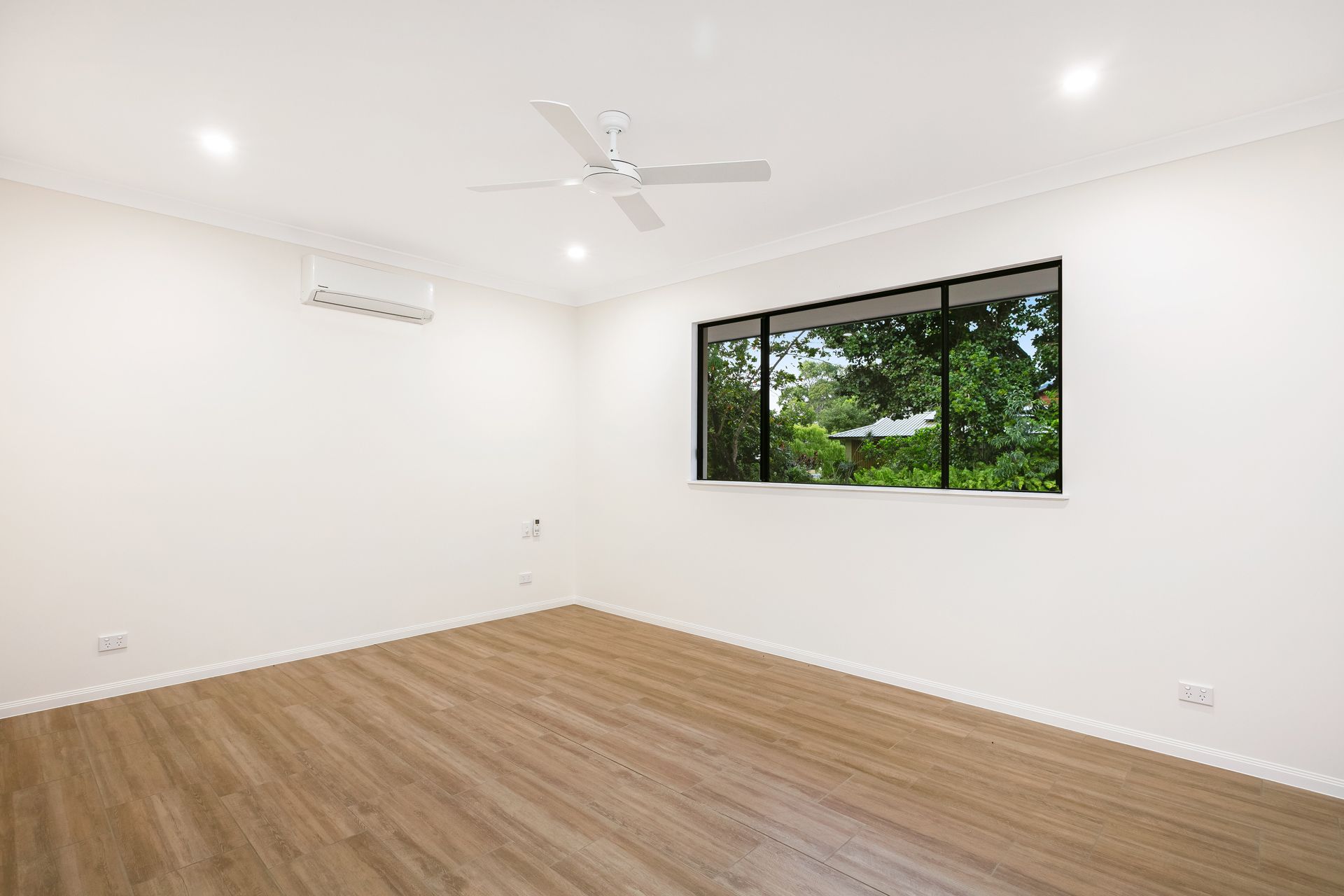 A Bright, Empty Room With White Walls, Light Wood-look Flooring, and a Ceiling Fan — Ashlee Jones Homes in Gordonvale, QLD