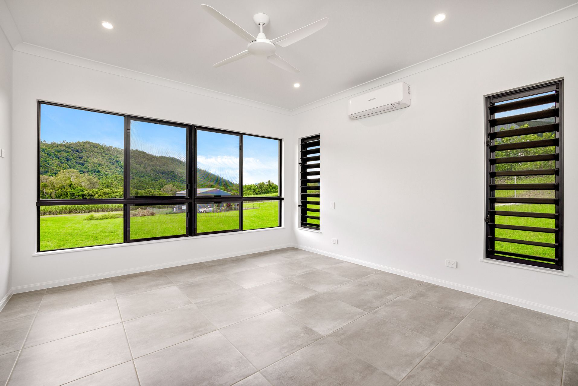 An Empty, Modern Room With Large Windows Showing a Green Hill — Ashlee Jones Homes in Gordonvale, QLD