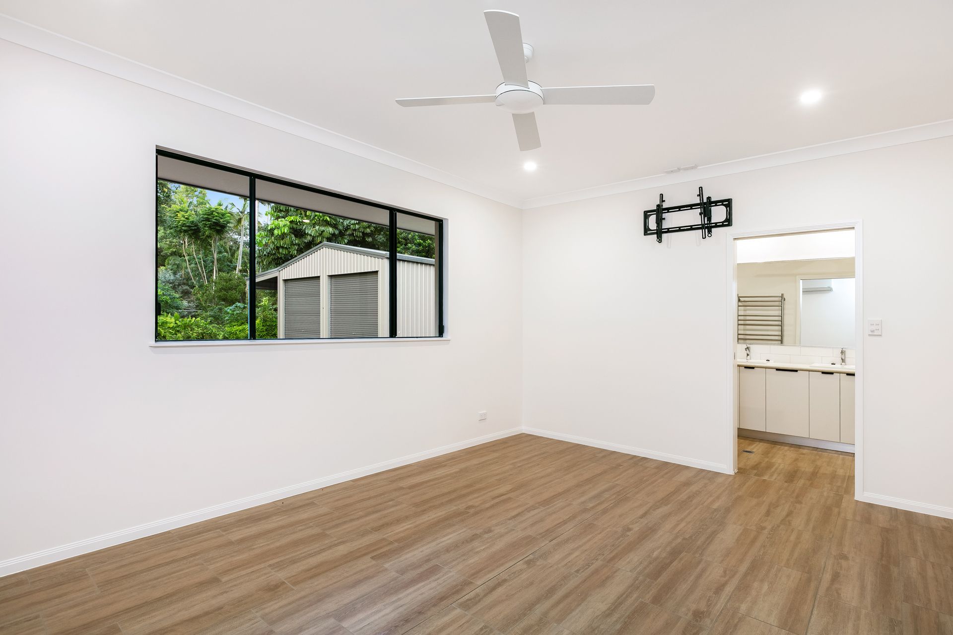 An Empty Room With White Walls, a Large Window, and Light Wood Flooring — Ashlee Jones Homes in Gordonvale, QLD