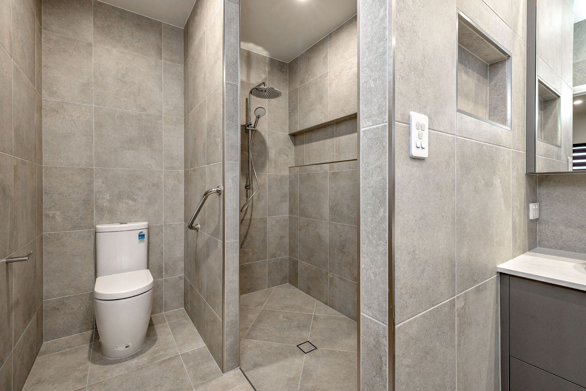 A Modern Bathroom Featuring a Walk-in Shower With Grey Stone Tiles — Ashlee Jones Homes in Gordonvale, QLD