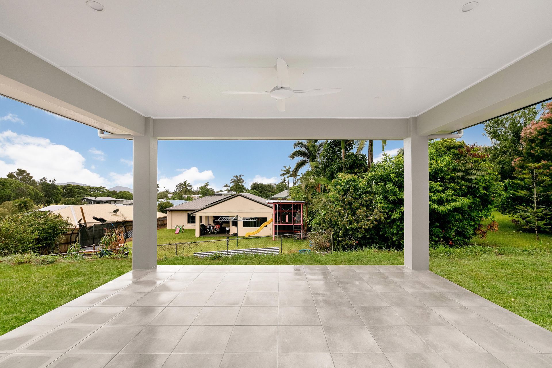 A Tiled Outdoor Patio With a Ceiling Fan, Overlooking a Grassy Backyard — Ashlee Jones Homes in Gordonvale, QLD