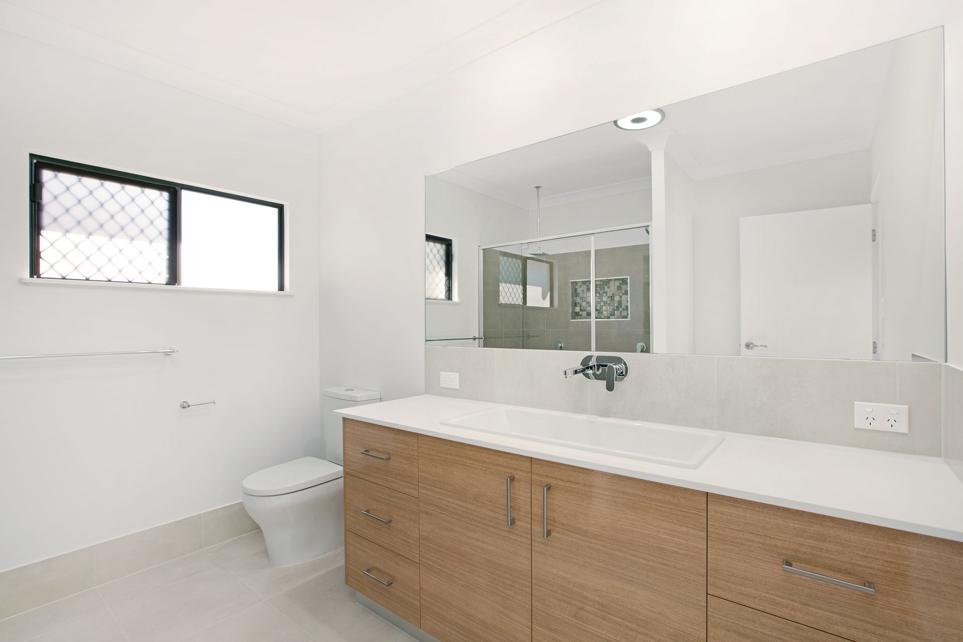 A Modern Bathroom With a Wood-toned Vanity, White Countertop — Ashlee Jones Homes in Gordonvale, QLD