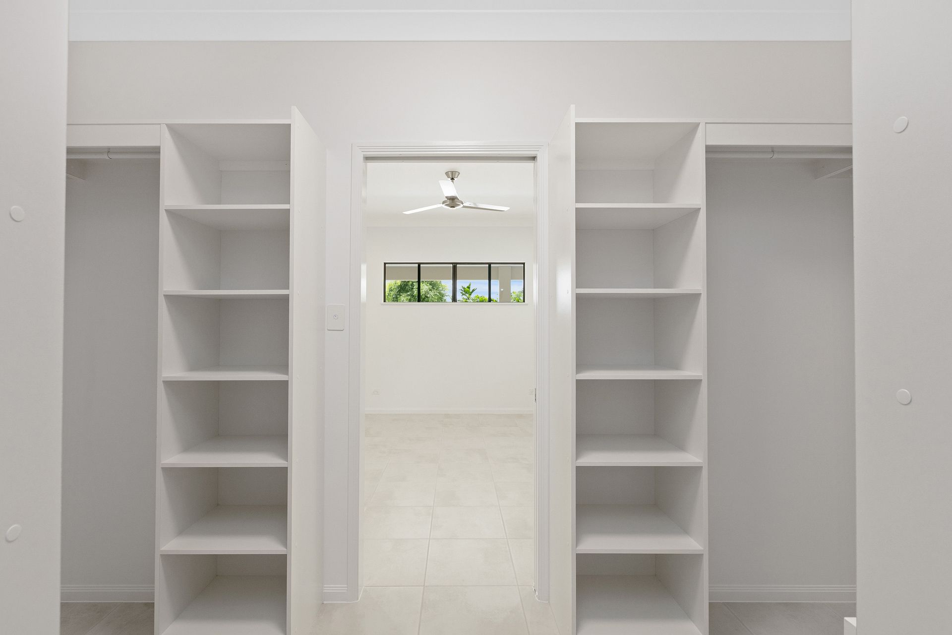 A Walk-through Closet With Symmetrical White Shelving Units on Both Sides — Ashlee Jones Homes in Gordonvale, QLD