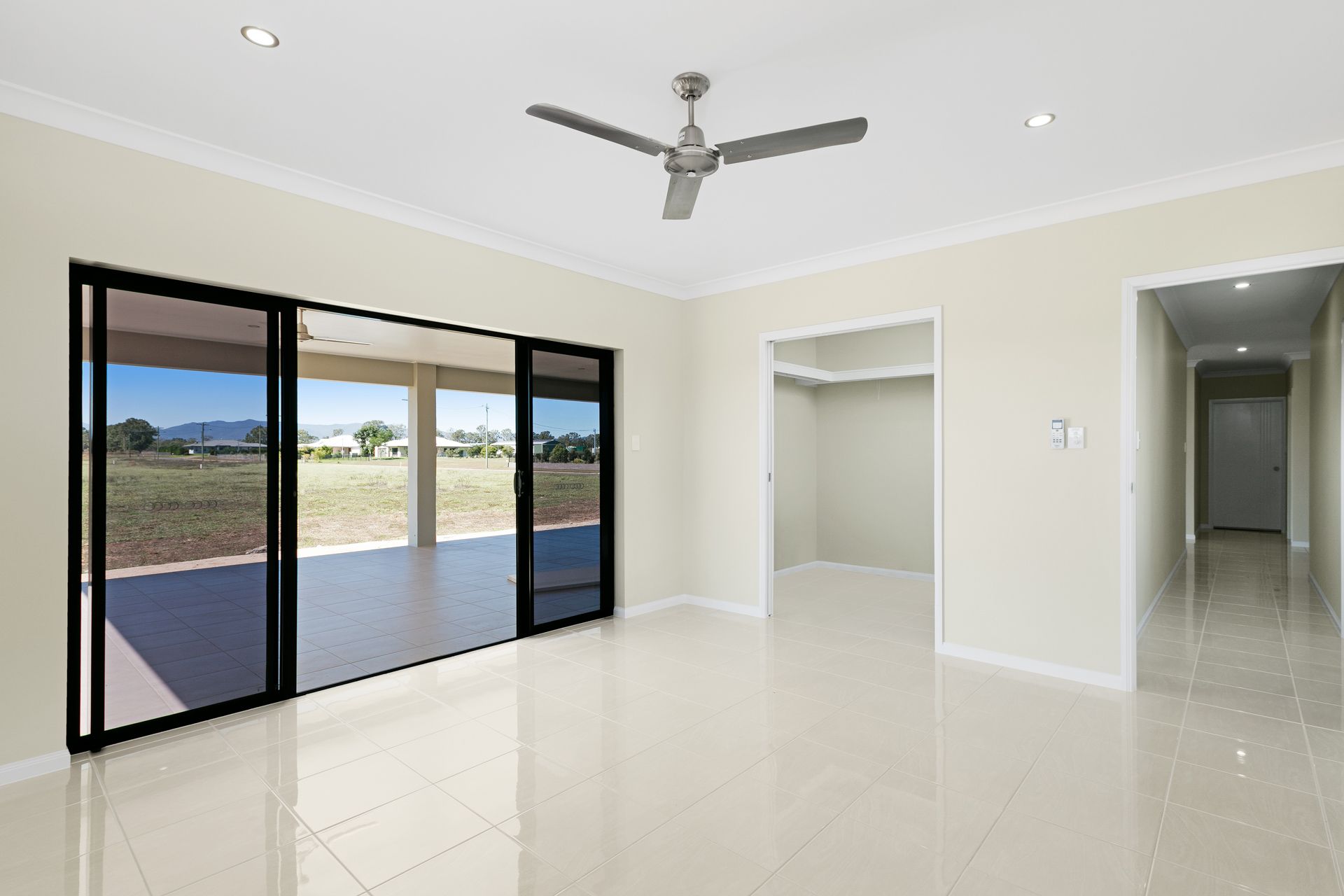 A Bright, Empty Living Room With Light-colored Tile Floors, a Ceiling Fan — Ashlee Jones Homes in Gordonvale, QLD
