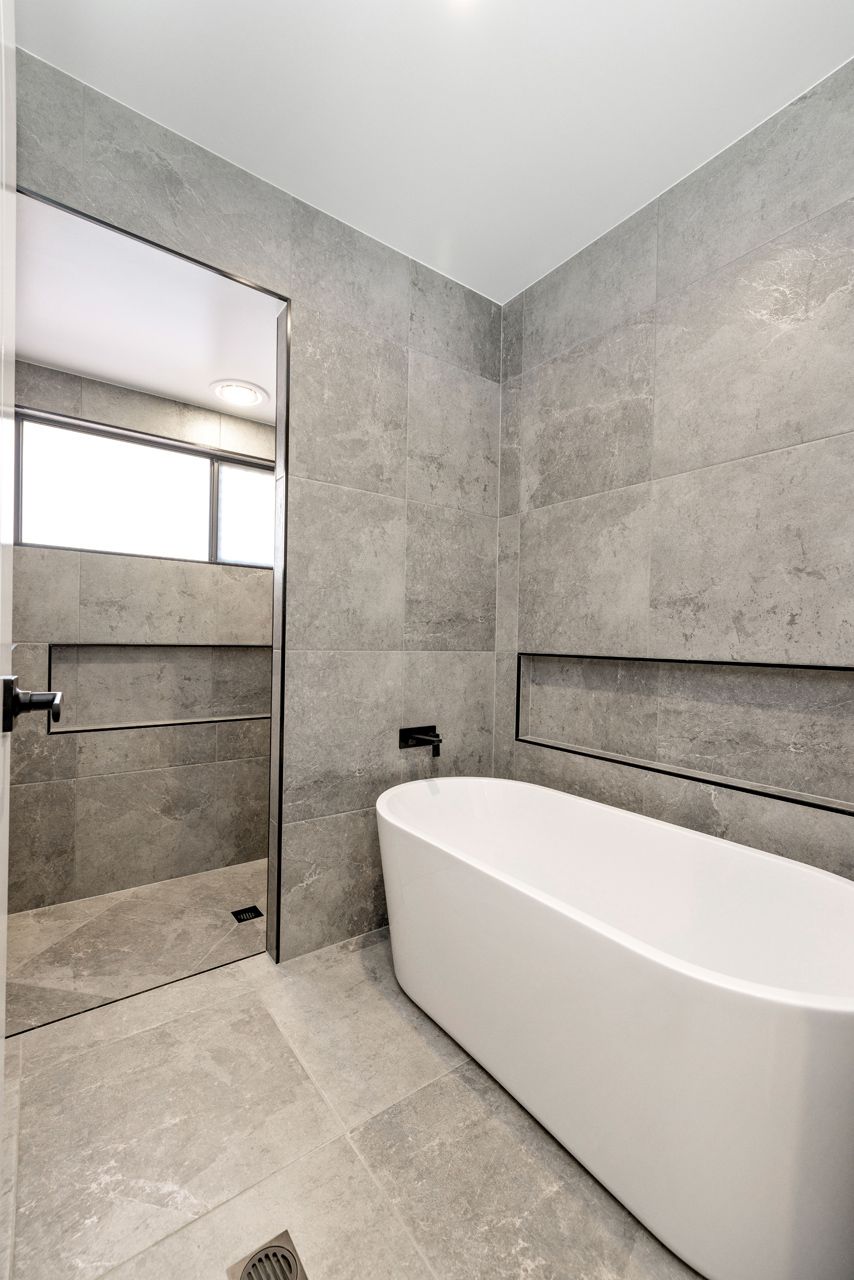 Modern Bathroom With Gray Stone Tiles, a White Freestanding Tub — Ashlee Jones Homes in Gordonvale, QLD
