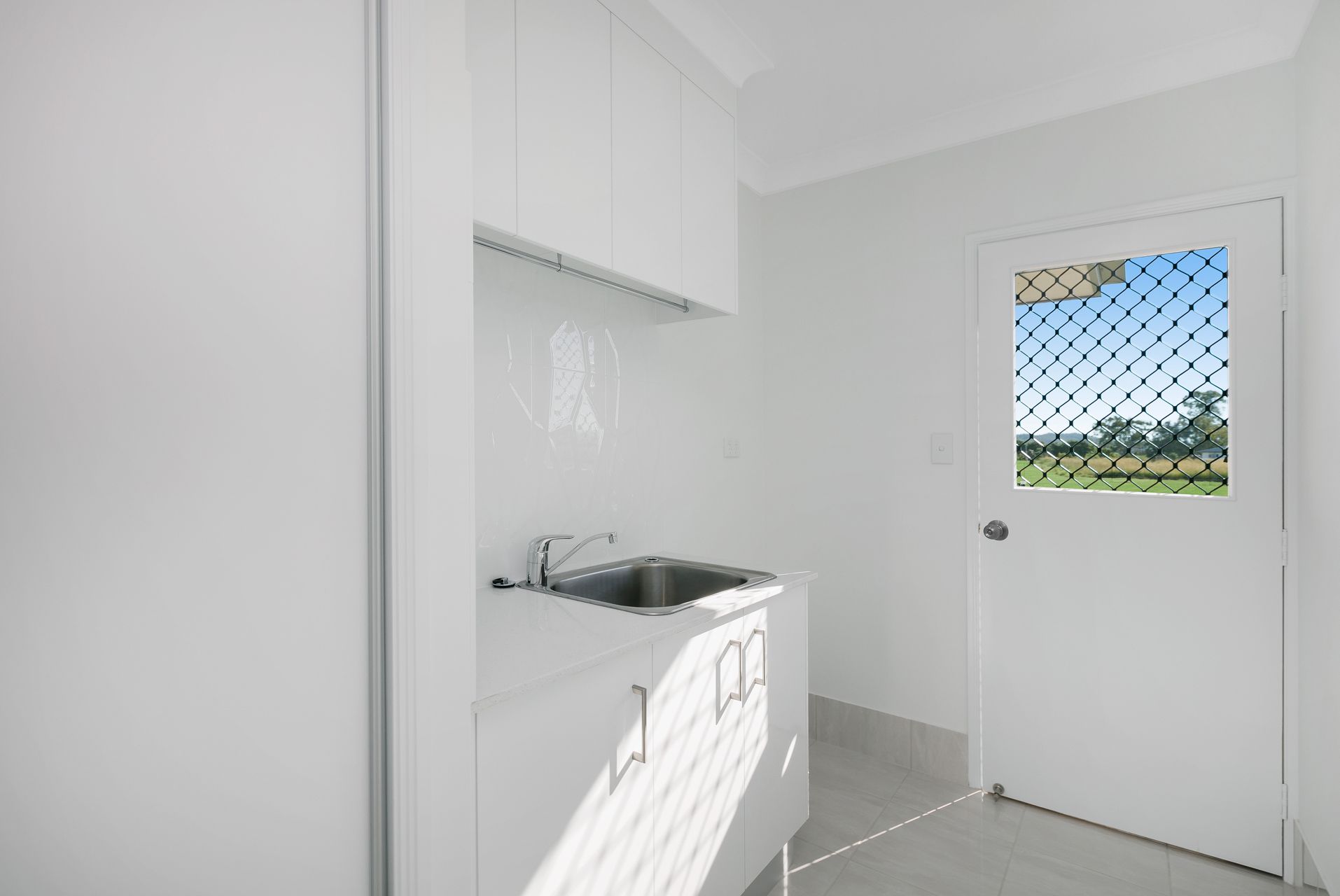 A Bright, Minimalist White Laundry Room Featuring a Sink — Ashlee Jones Homes in Gordonvale, QLD
