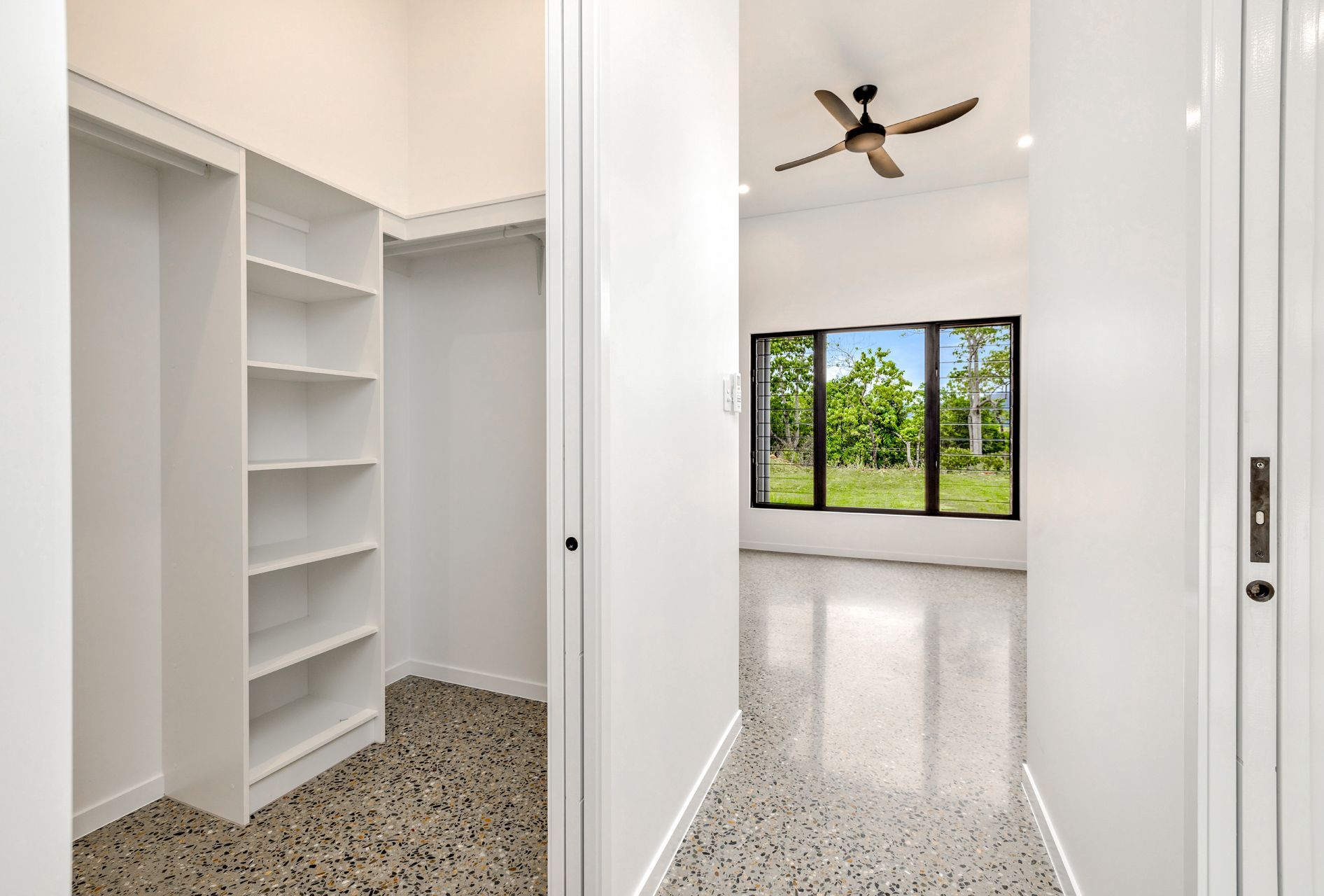A Walk-in Closet With White Shelving Beside a Hallway Leading to a Room — Ashlee Jones Homes in Gordonvale, QLD