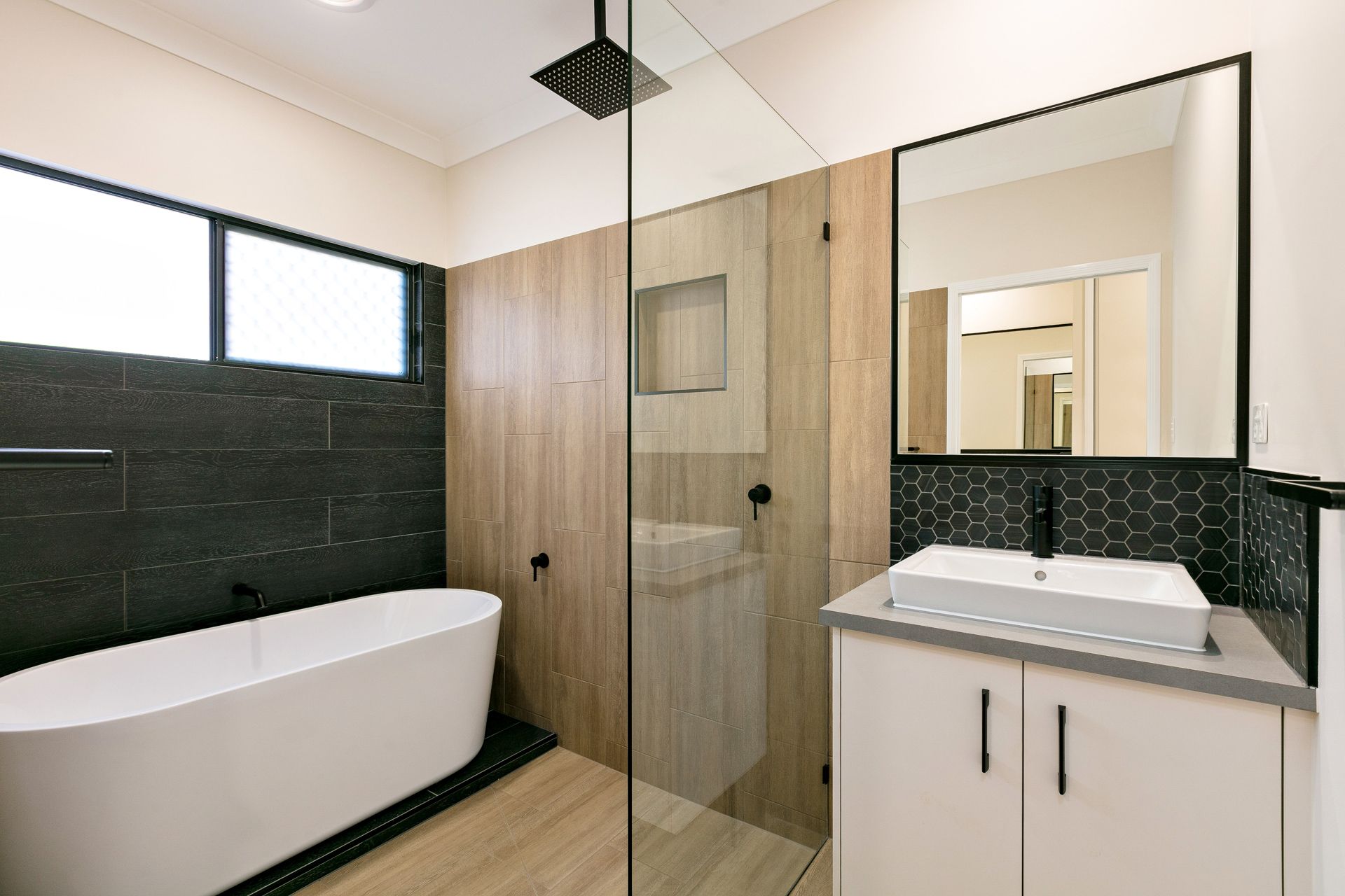 A Modern Bathroom Featuring a White Soaking Tub Against Dark Tile — Ashlee Jones Homes in Gordonvale, QLD