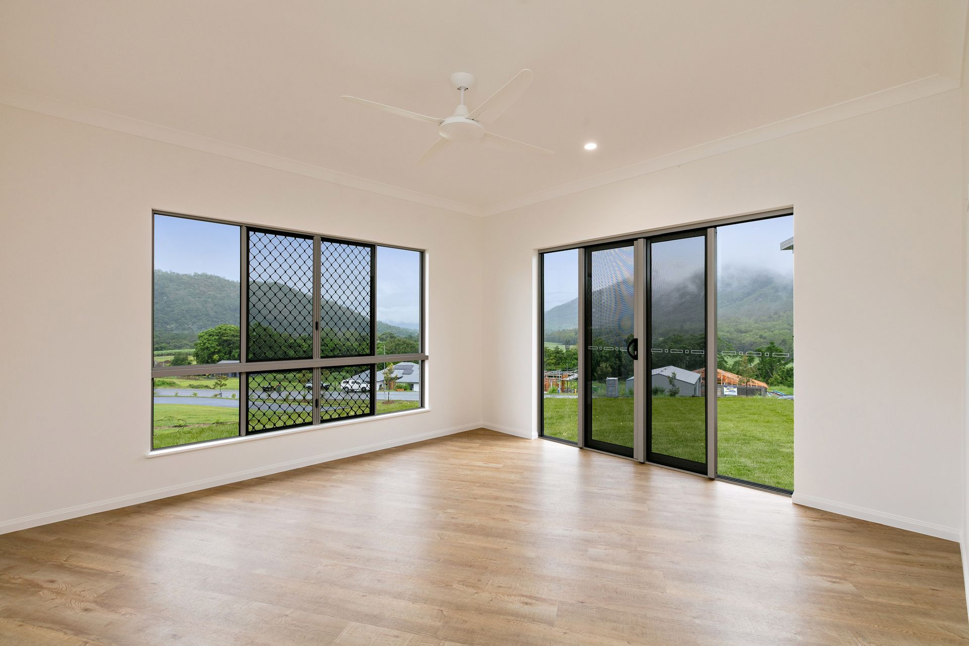 A Bright, Empty Living Room With Wood-look Flooring, White Walls — Ashlee Jones Homes in Gordonvale, QLD