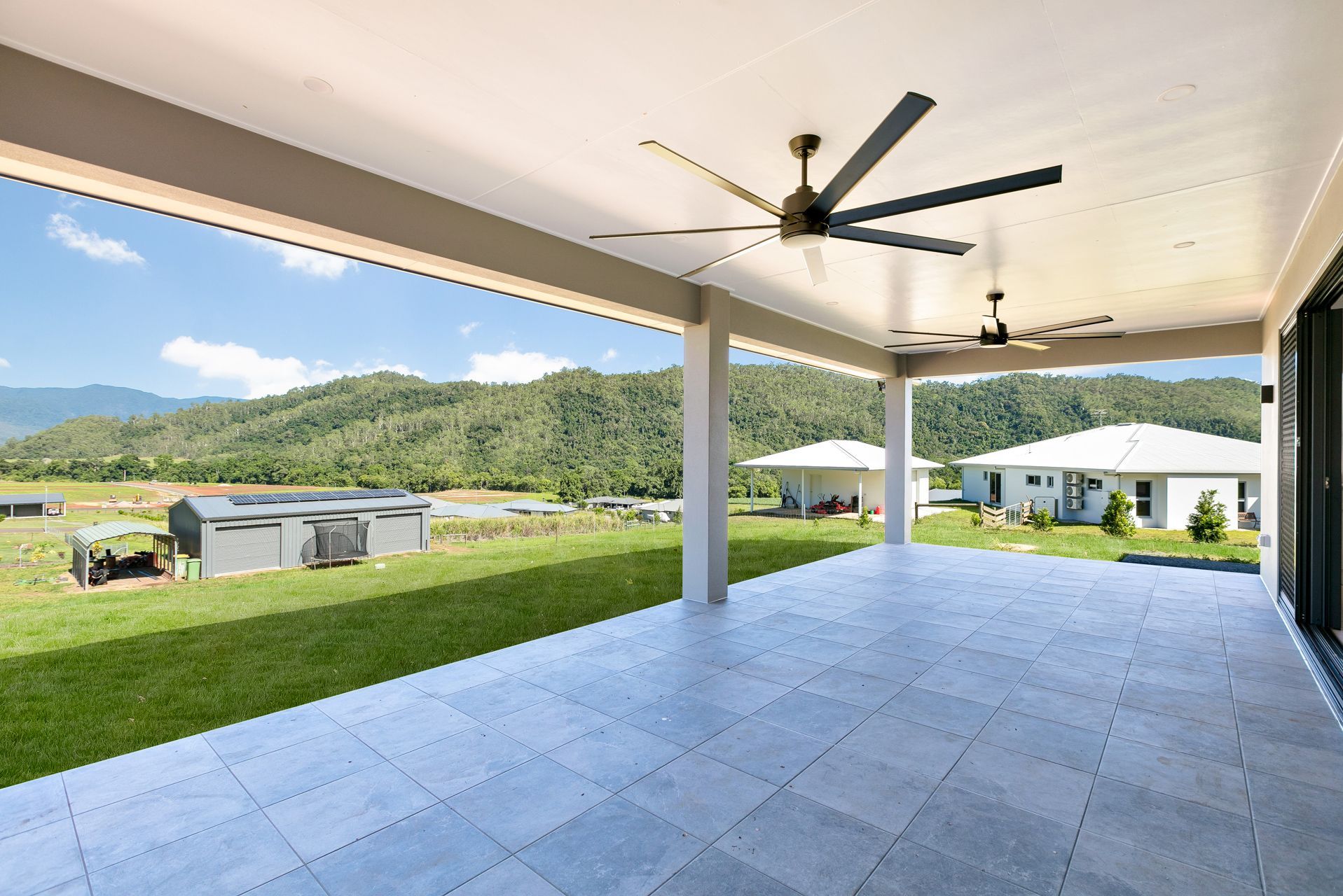 A Tiled Patio With Two Ceiling Fans Looks Out Over a Grassy Field — Ashlee Jones Homes in Gordonvale, QLD