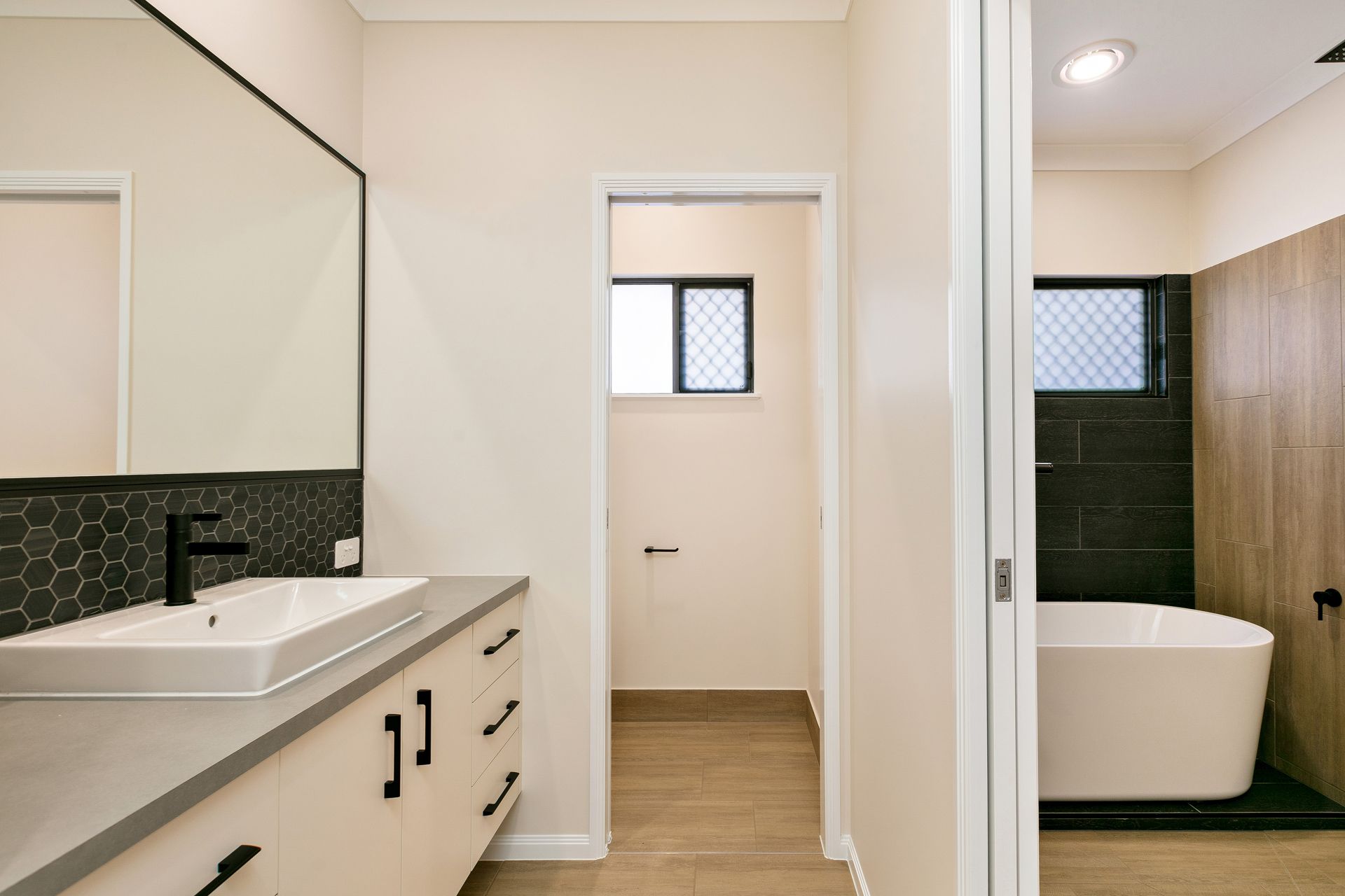 A Modern Bathroom Featuring a White Vanity With Black Hardware — Ashlee Jones Homes in Gordonvale, QLD