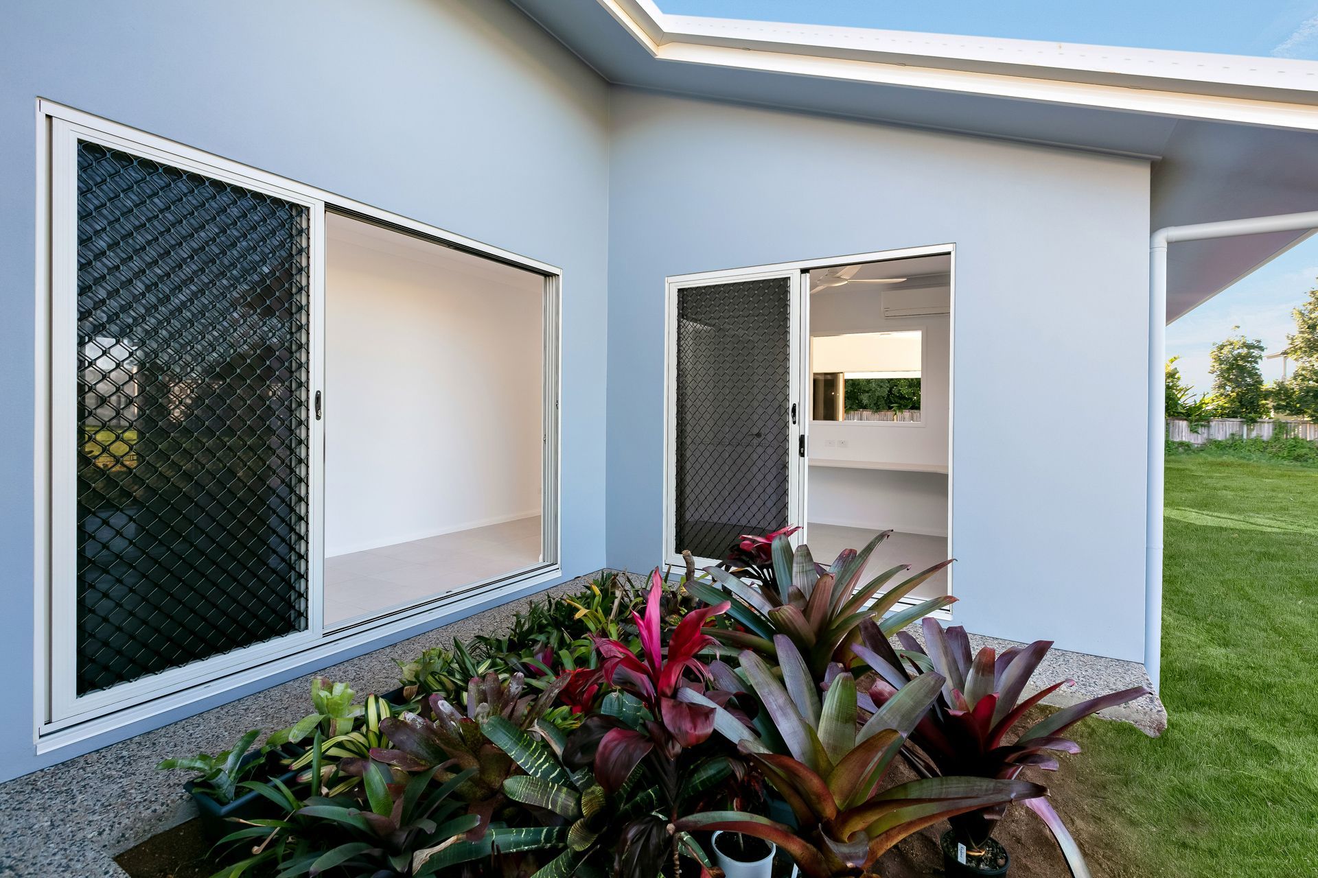 A Light Blue House With Large Sliding Glass Doors and Security Screens — Ashlee Jones Homes in Gordonvale, QLD