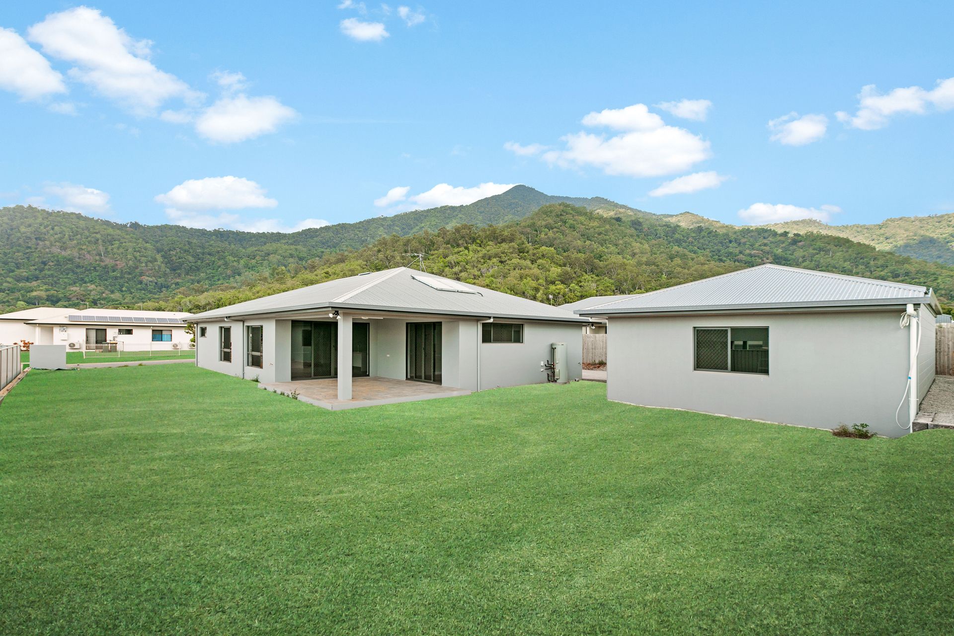 A Grassy Backyard With Two Modern, Single-story Light Gray Houses — Ashlee Jones Homes in Gordonvale, QLD