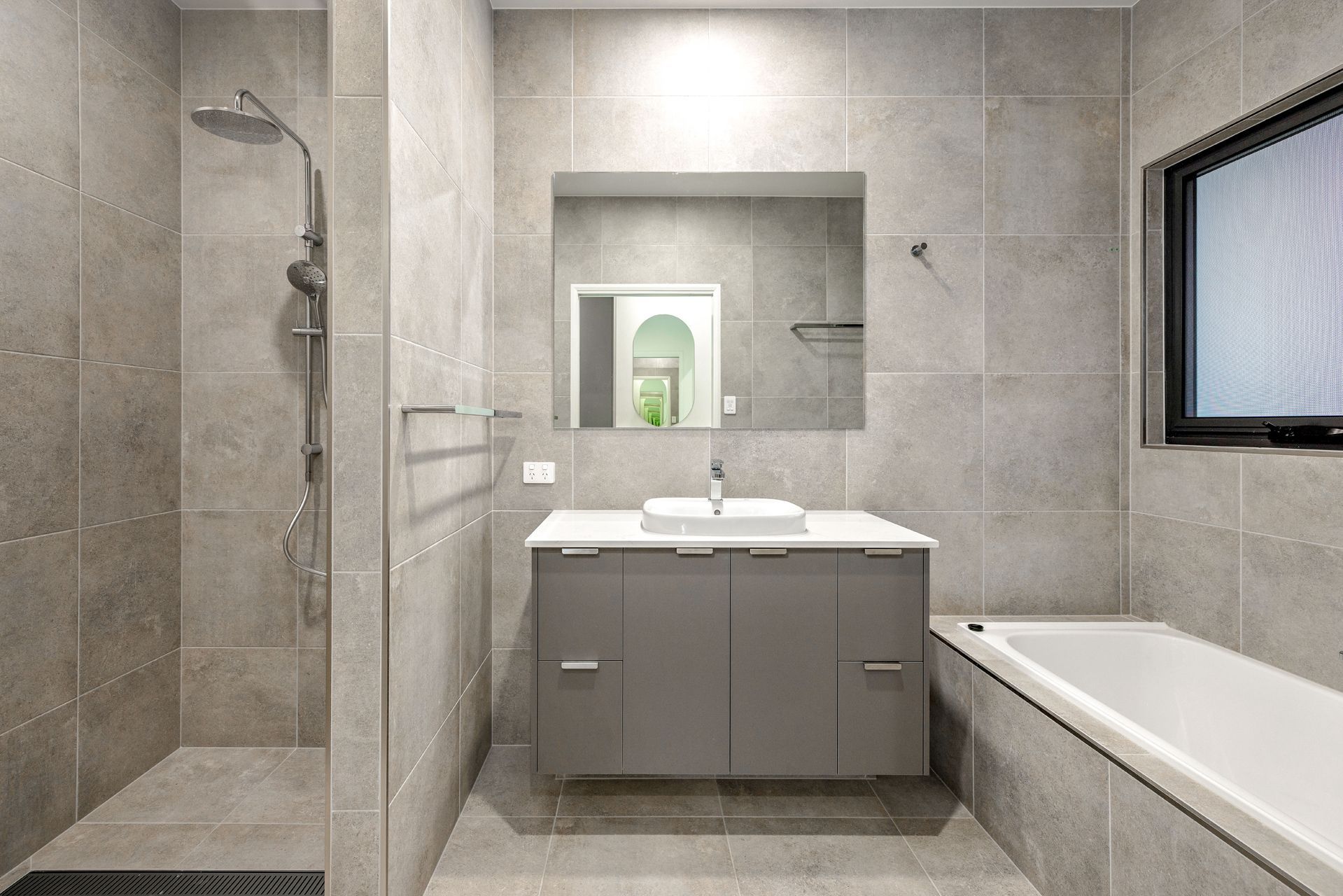 A Modern Gray-tiled Bathroom Featuring a Walk-in Shower — Ashlee Jones Homes in Gordonvale, QLD