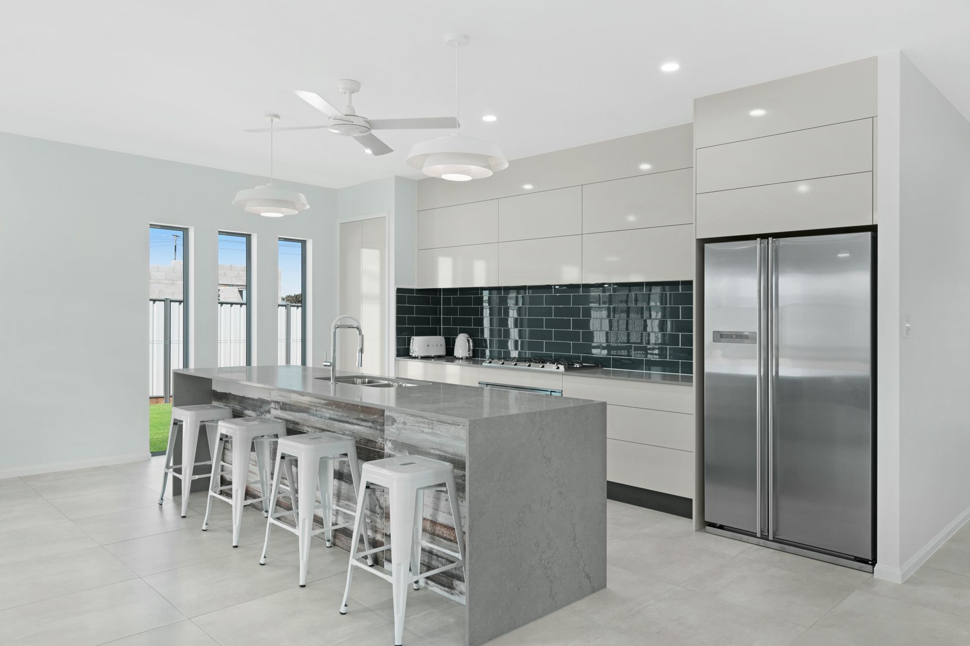 A Modern Kitchen Featuring a Gray Stone Island With Four White Stools — Ashlee Jones Homes in Gordonvale, QLD