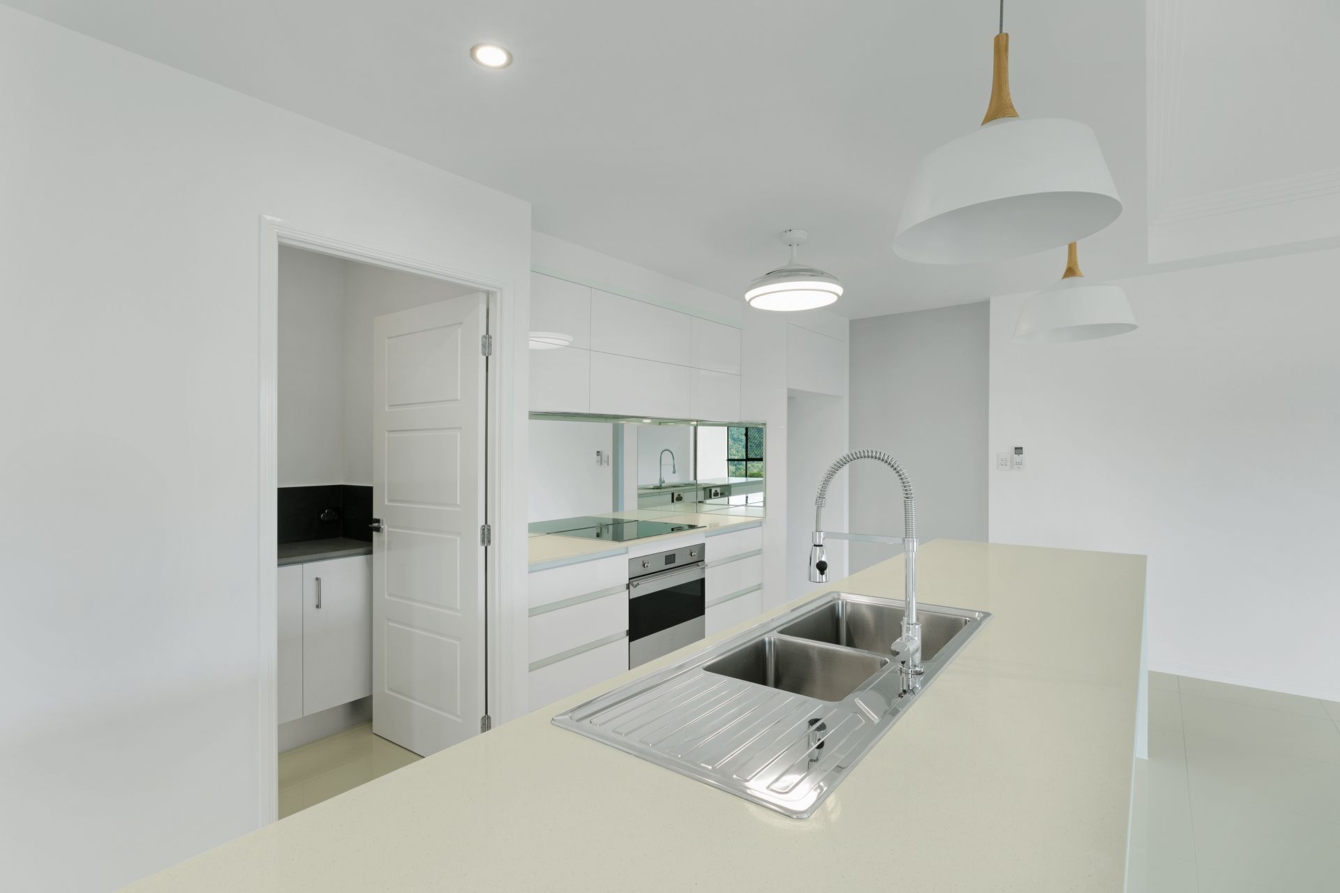 A Modern, White Kitchen Featuring a Large Island With a Stainless Steel Sink — Ashlee Jones Homes in Gordonvale, QLD
