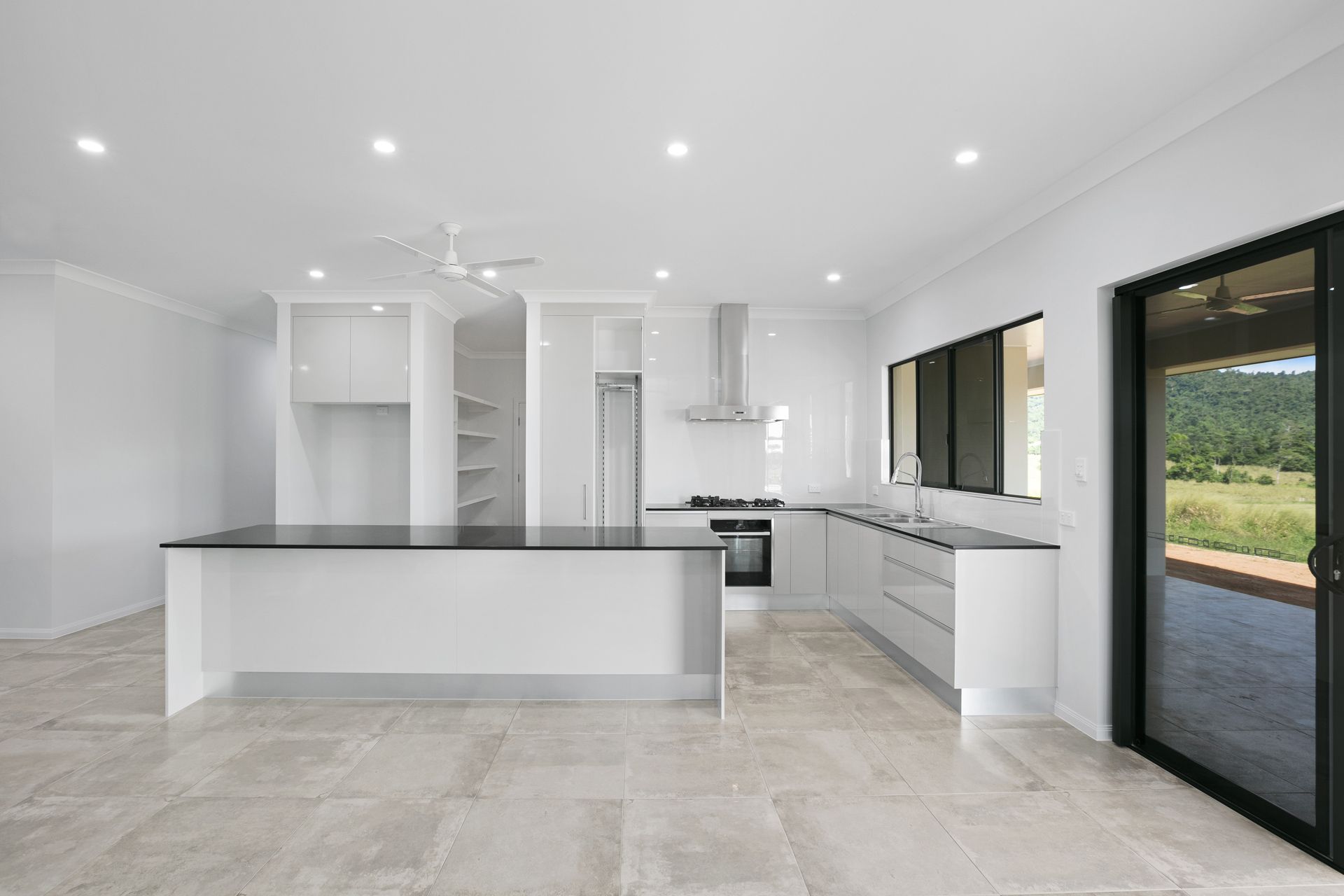 A Modern White Kitchen Featuring a Long Island With a Black Countertop — Ashlee Jones Homes in Gordonvale, QLD