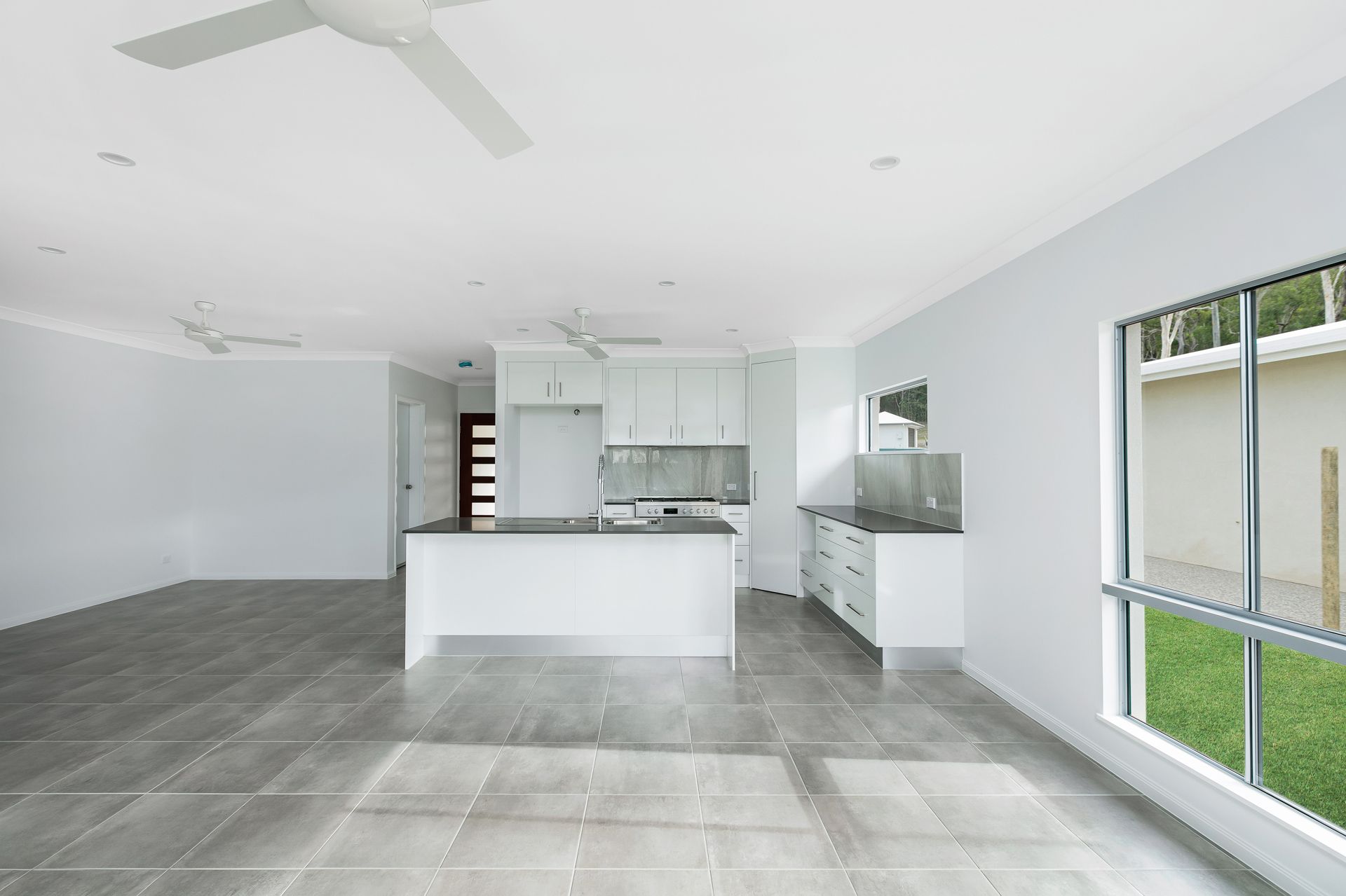 A Modern, Open-plan Kitchen and Living Space With Grey Tiled Floors — Ashlee Jones Homes in Gordonvale, QLD