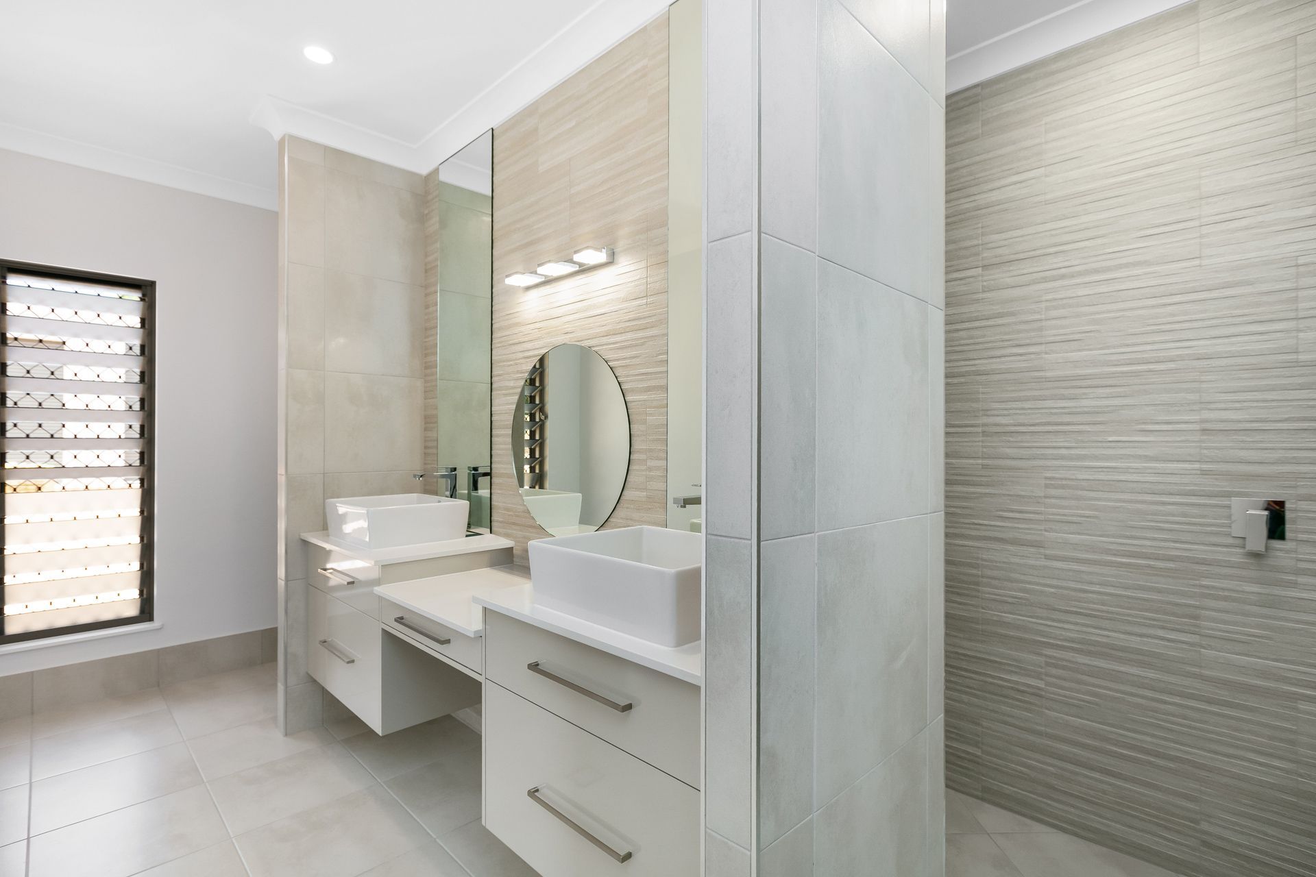 Modern Bathroom With a Double Vanity, Round Mirror — Ashlee Jones Homes in Gordonvale, QLD