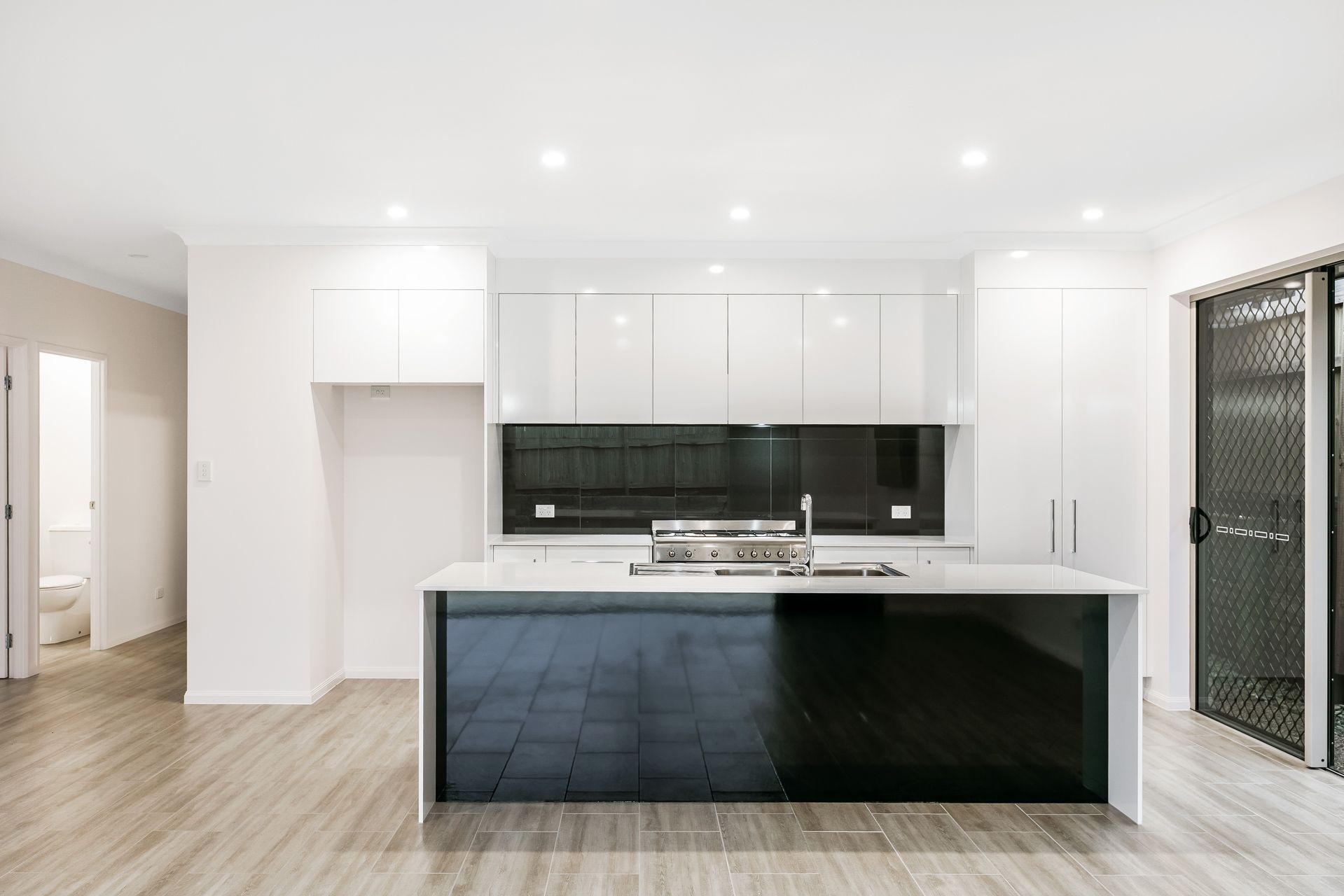 A Modern Kitchen With White Cabinets, a Black Backsplash, a Black Kitchen Island — Ashlee Jones Homes in Gordonvale, QLD