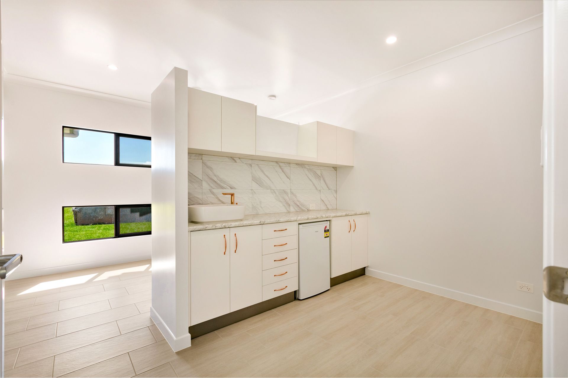 A Minimalist Kitchenette Featuring White Cabinets, a Marble Backsplash — Ashlee Jones Homes in Gordonvale, QLD