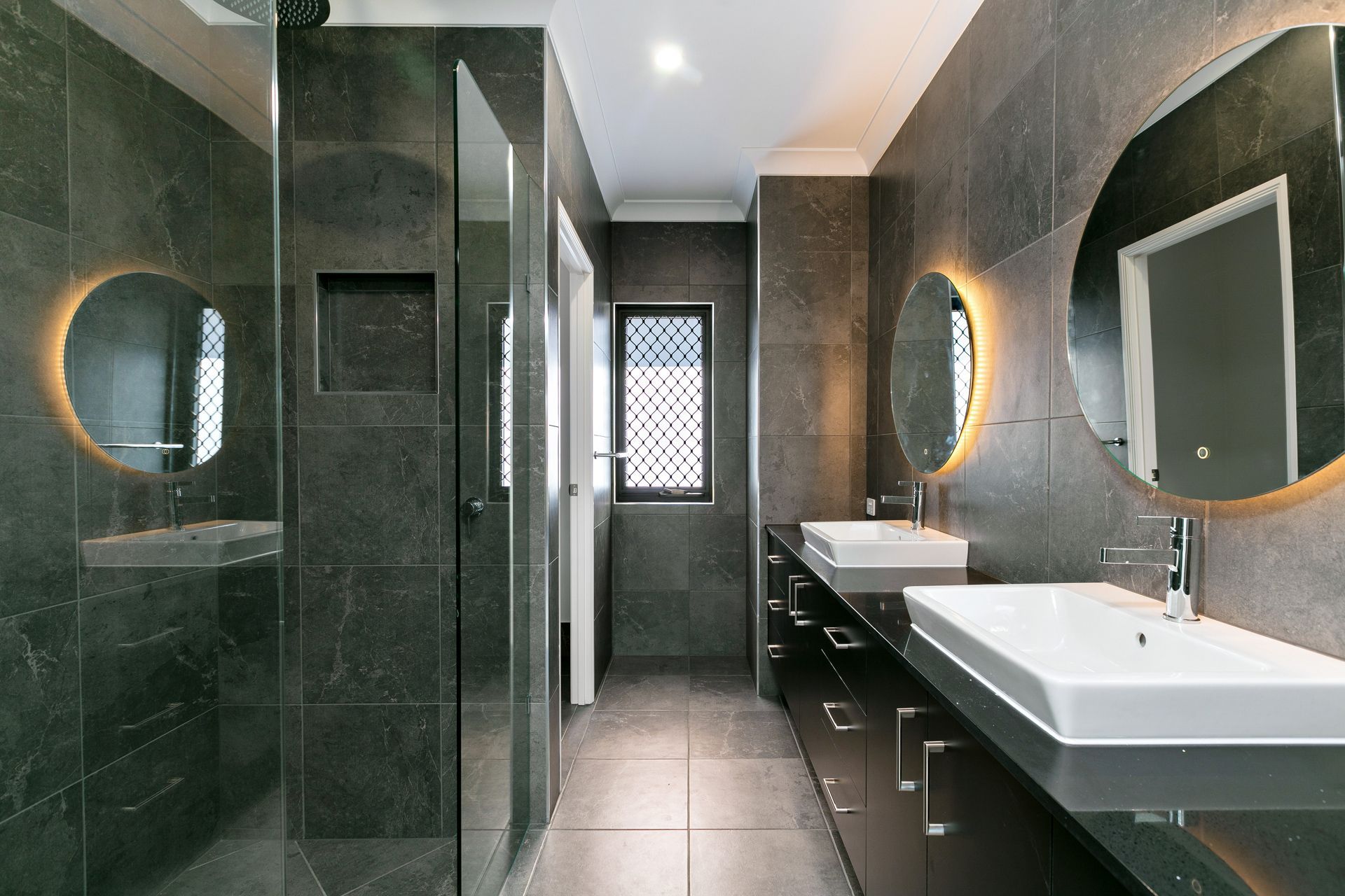 A Modern Bathroom With Dark Stone Tiles, a Glass Shower — Ashlee Jones Homes in Gordonvale, QLD
