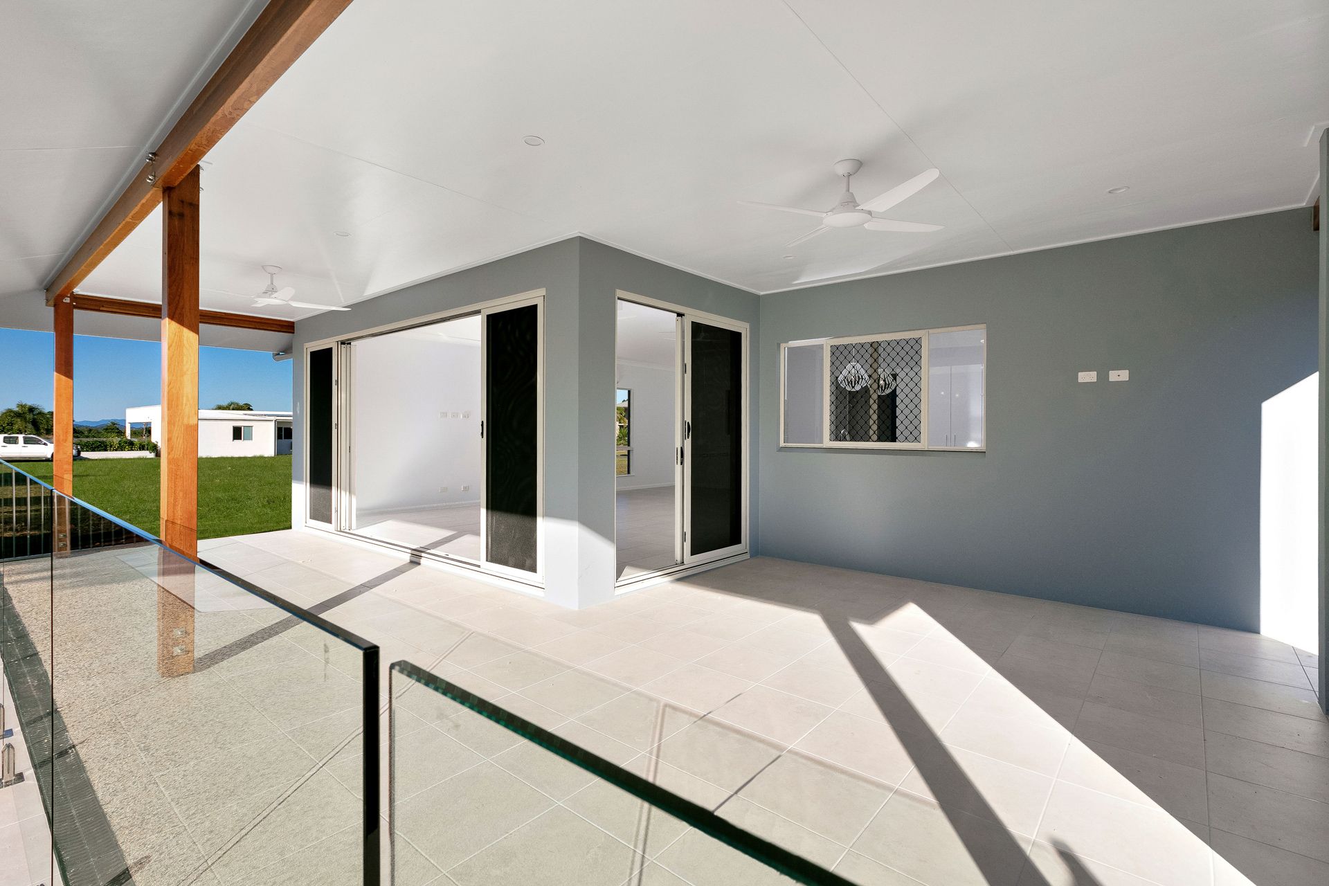 A Modern Patio With Light Grey Tiles, a Glass Railing — Ashlee Jones Homes in Gordonvale, QLD