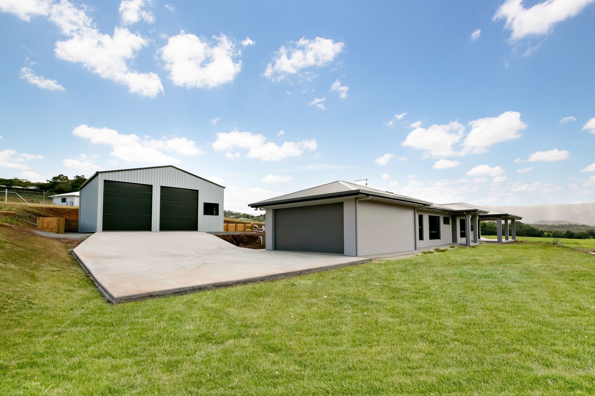 A Grey Suburban House and a Detached Matching Shed on a Concrete Driveway — Ashlee Jones Homes in Gordonvale, QLD