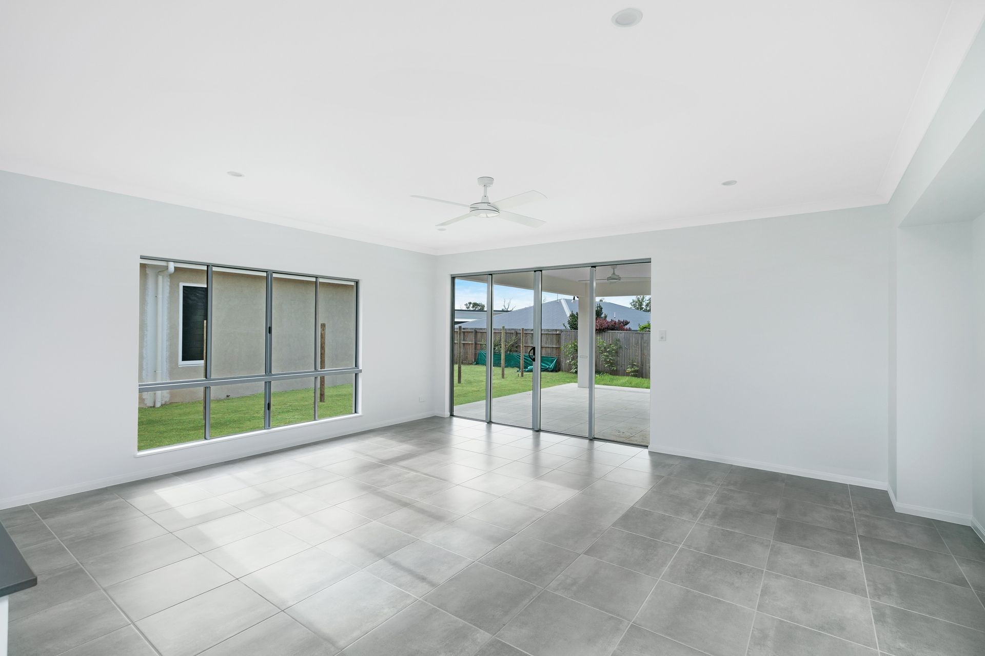 A Spacious, Bright, Empty Room With Grey Tiled Floors — Ashlee Jones Homes in Gordonvale, QLD