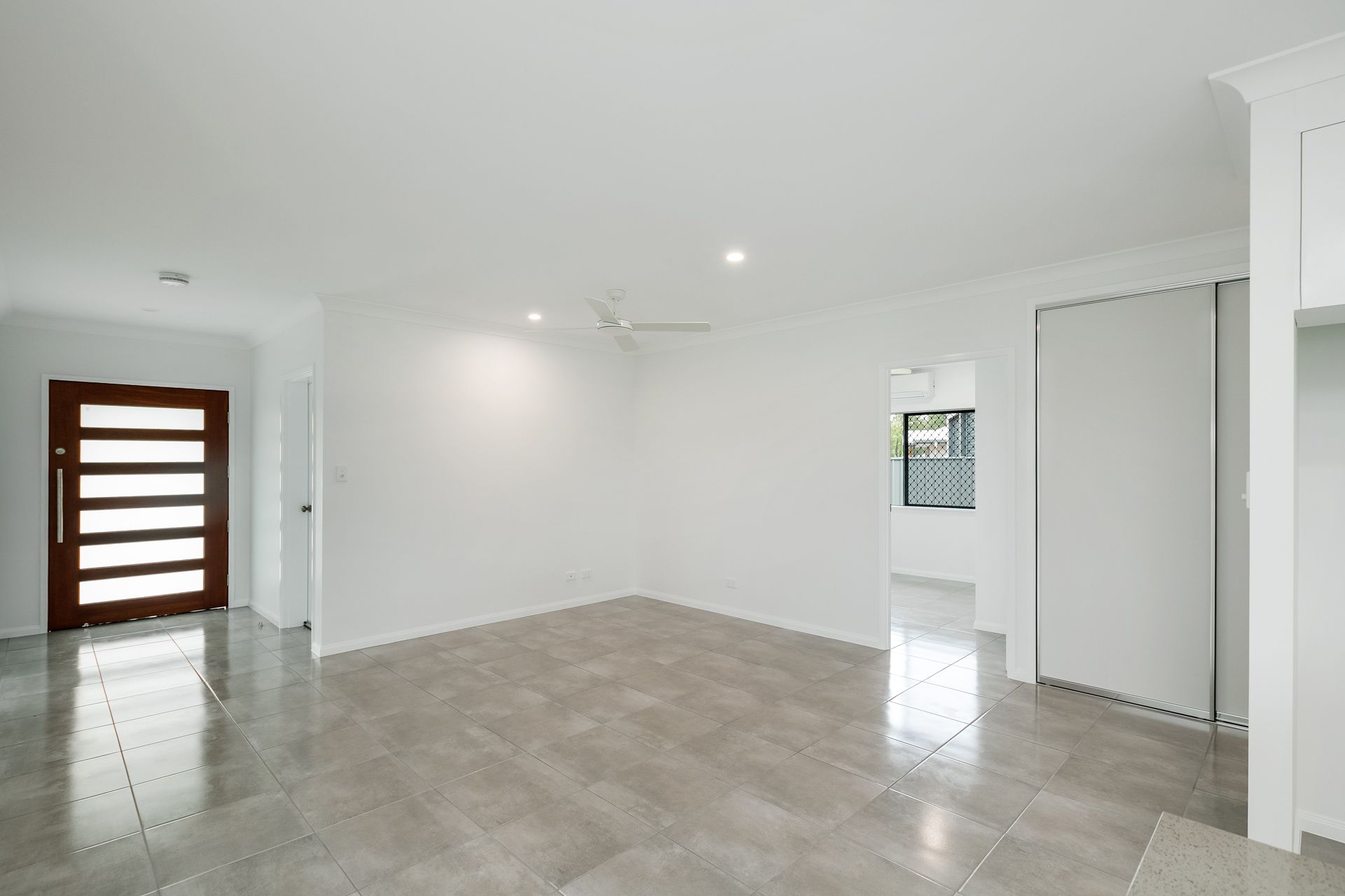 A Bright, Empty Living Room With Light Gray Tile Flooring — Ashlee Jones Homes in Gordonvale, QLD