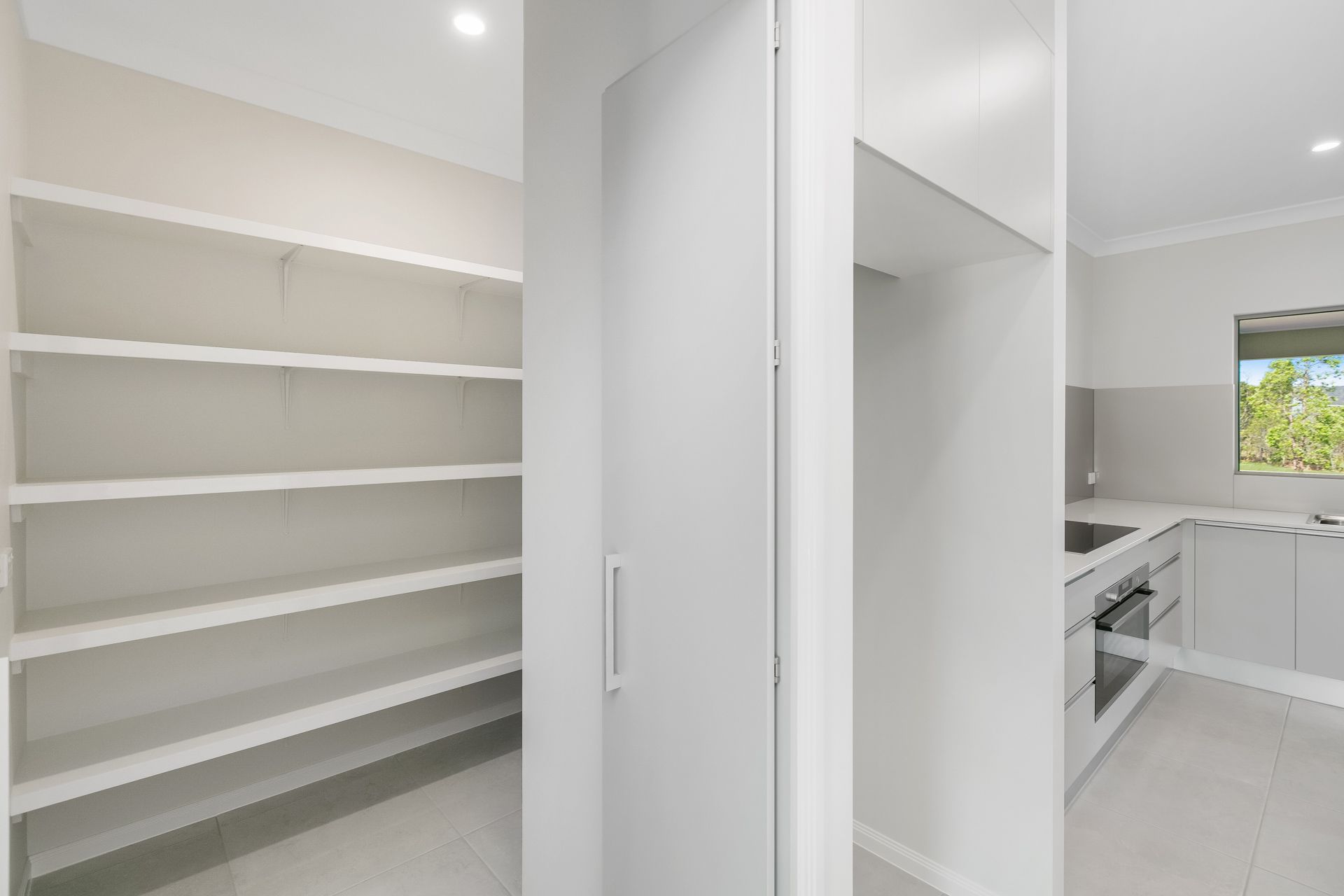 A Modern White Pantry With Empty Shelves Next to a Minimalist Kitchen — Ashlee Jones Homes in Gordonvale, QLD