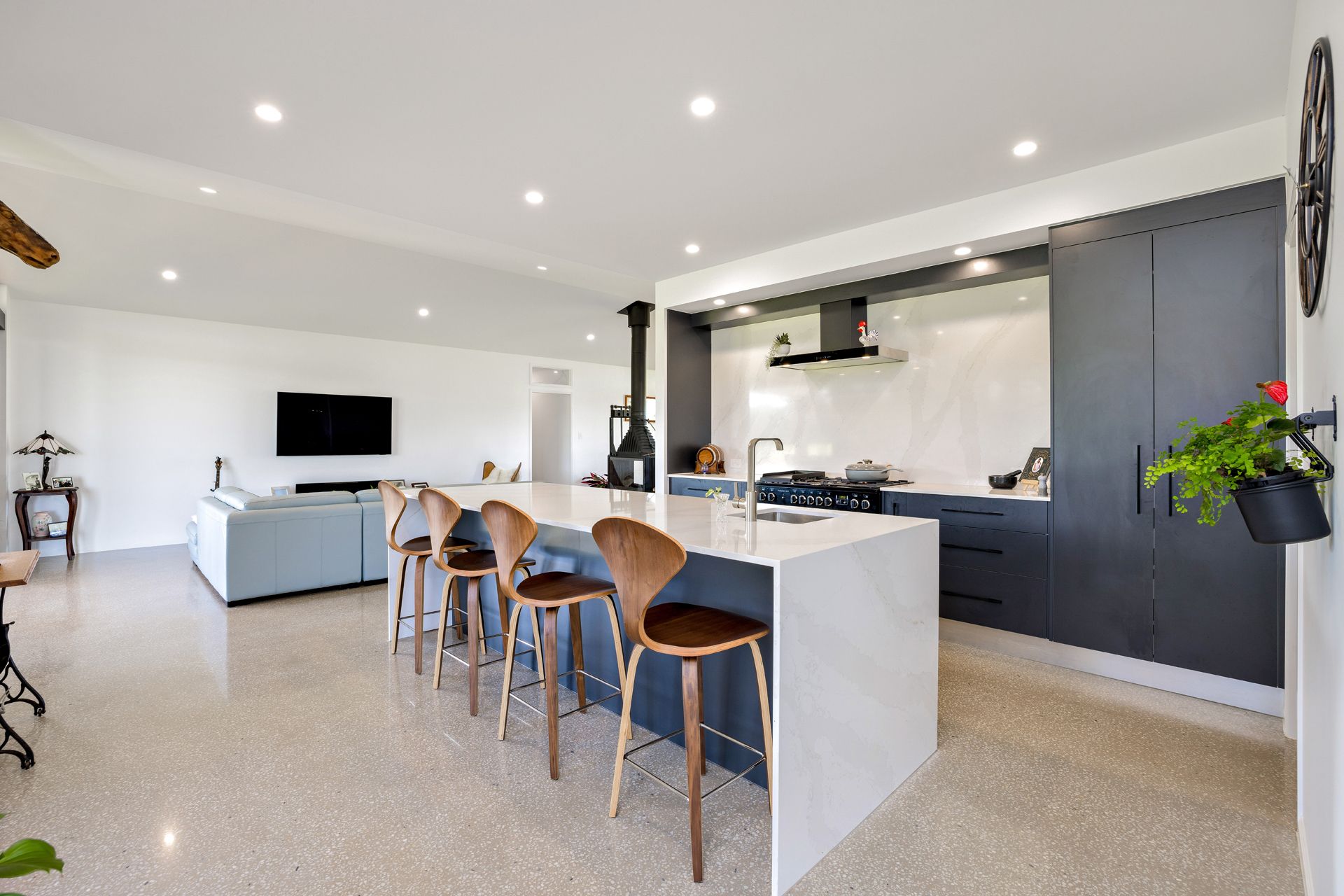 A Modern Open-plan Kitchen Featuring a Long White Island With Wooden Stools — Ashlee Jones Homes in Gordonvale, QLD