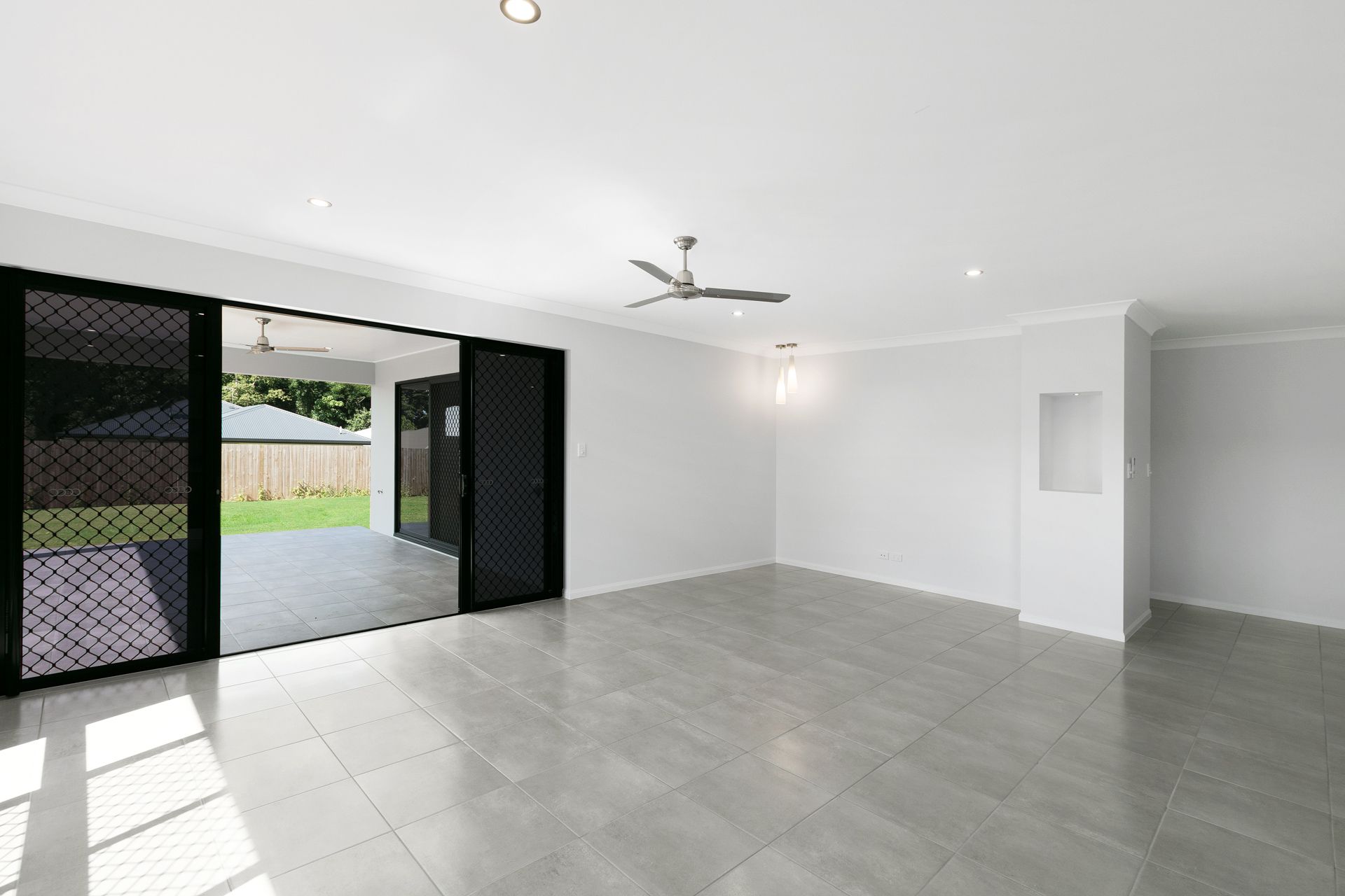 A Bright, Empty Living Room With Light Gray Tile Floors — Ashlee Jones Homes in Gordonvale, QLD