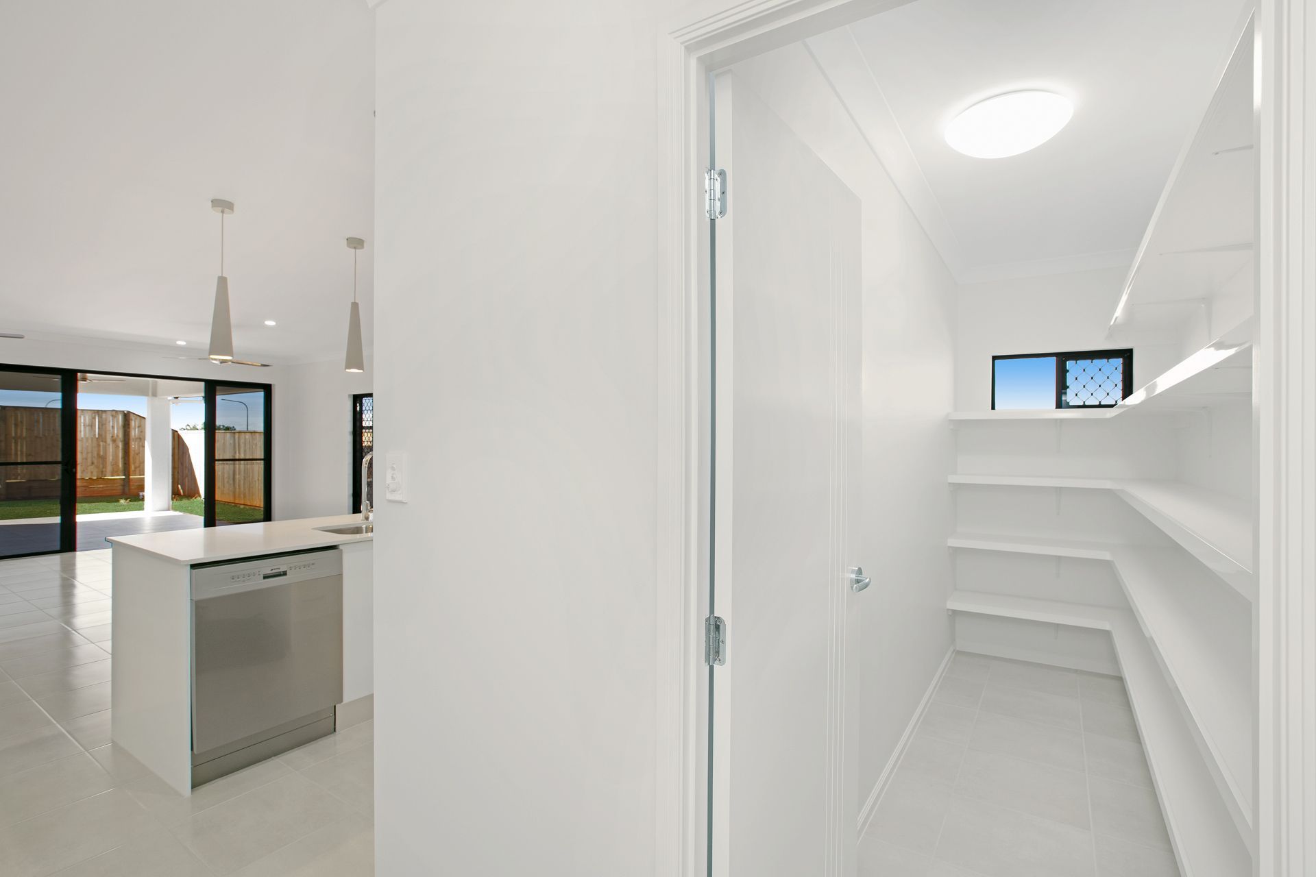 A Walk-in Pantry With White Shelves Beside an Open-plan Kitchen — Ashlee Jones Homes in Gordonvale, QLD