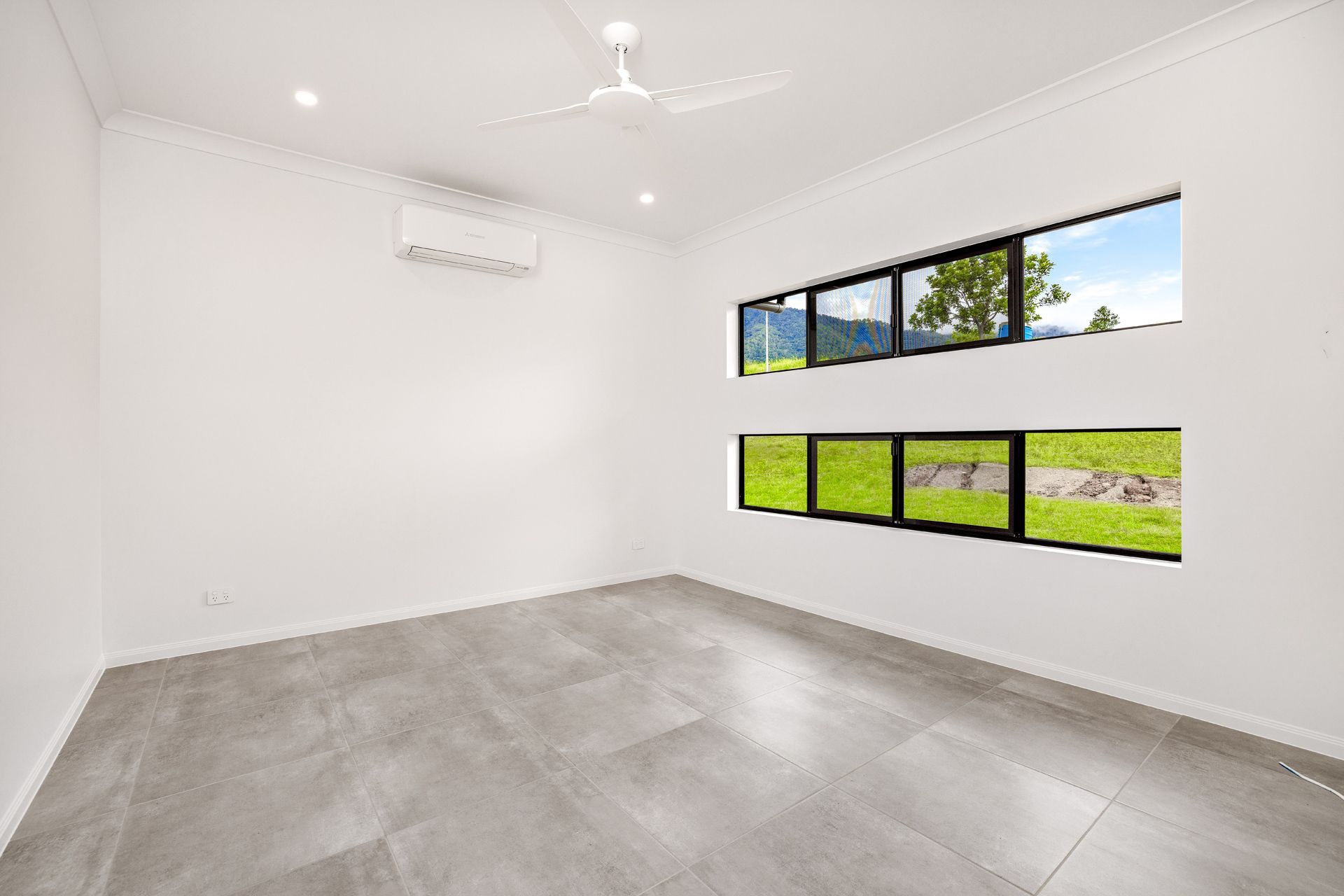 An Empty Room With White Walls, Large Rectangular Windows, Grey Tiled Floors — Ashlee Jones Homes in Gordonvale, QLD