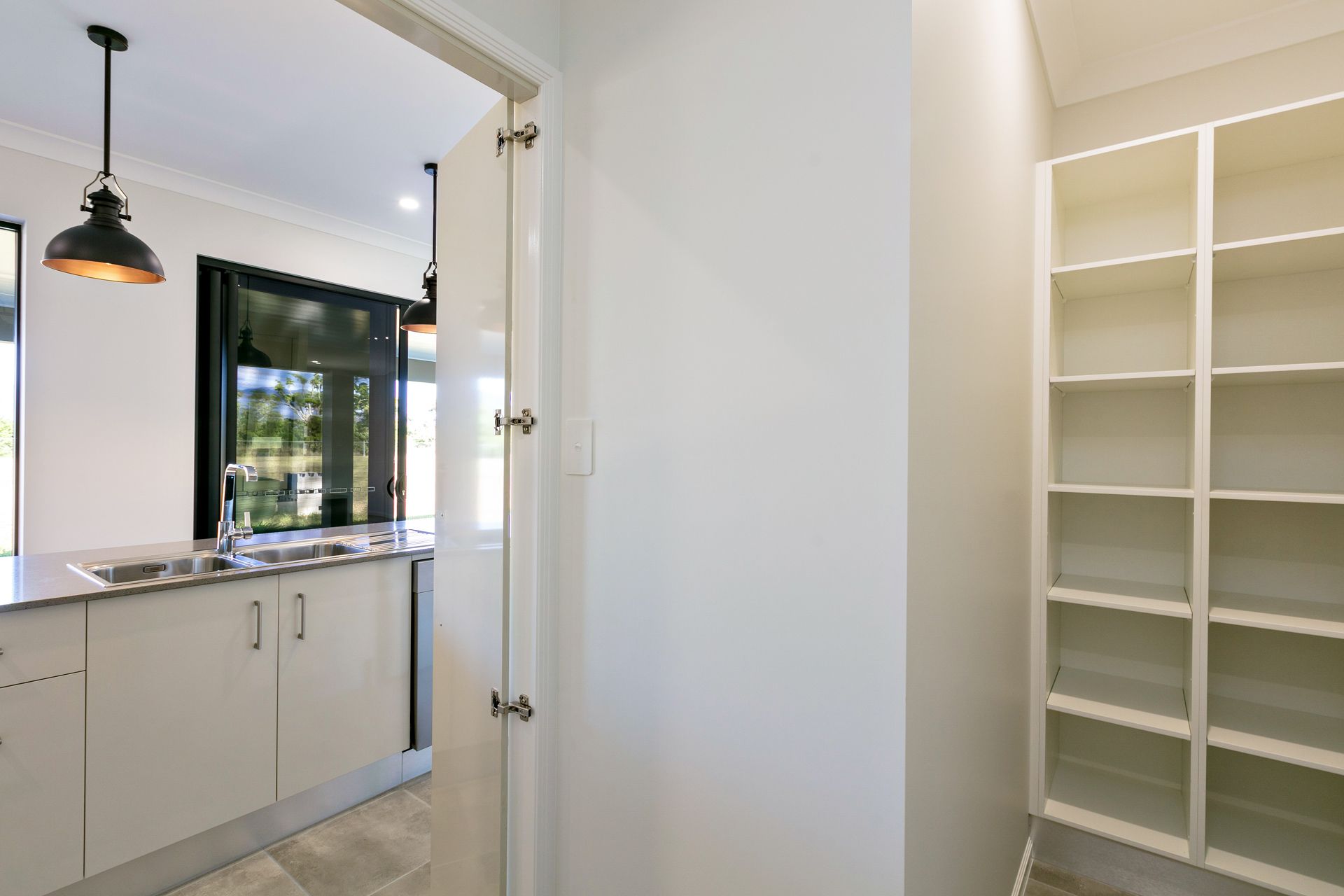 A Bright Walk-in Pantry With White Shelving Beside a Doorway — Ashlee Jones Homes in Gordonvale, QLD