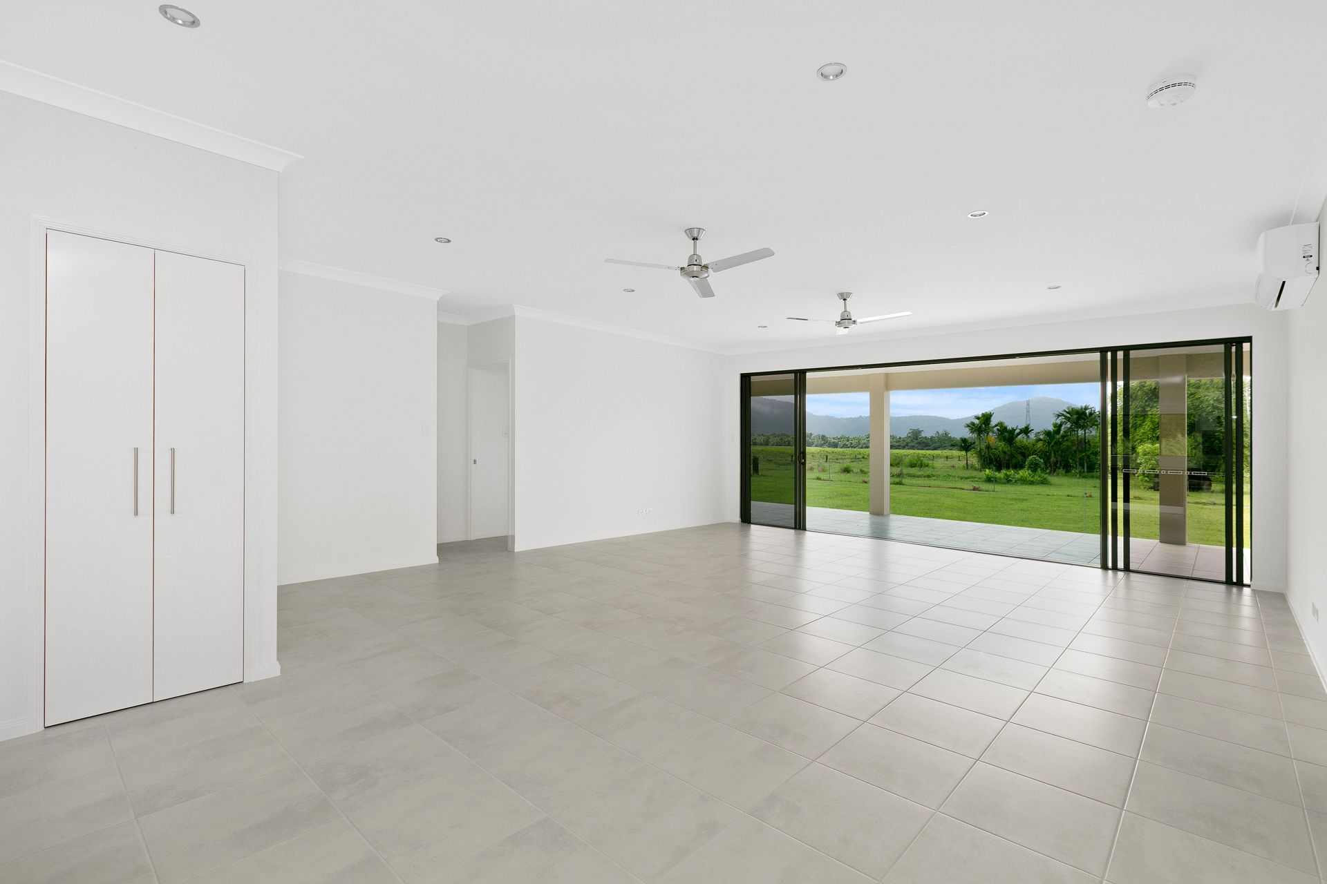 A Bright, Empty Living Room With Light Gray Tile Flooring — Ashlee Jones Homes in Gordonvale, QLD